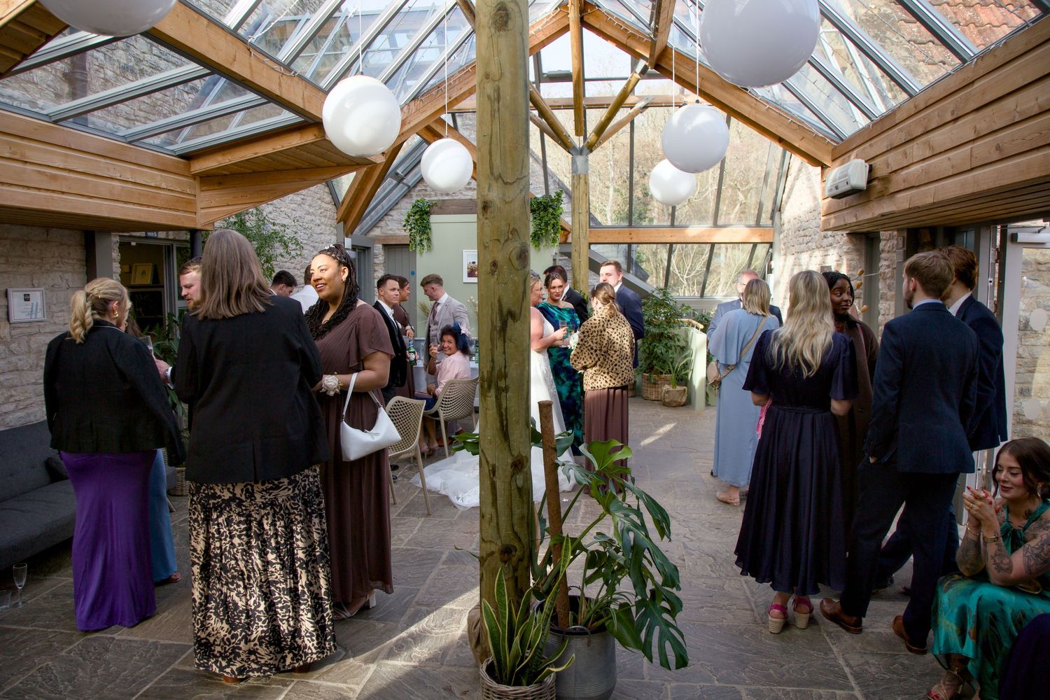 Wedding guests mingle in covered outdoor reception area decorated with white balloons.