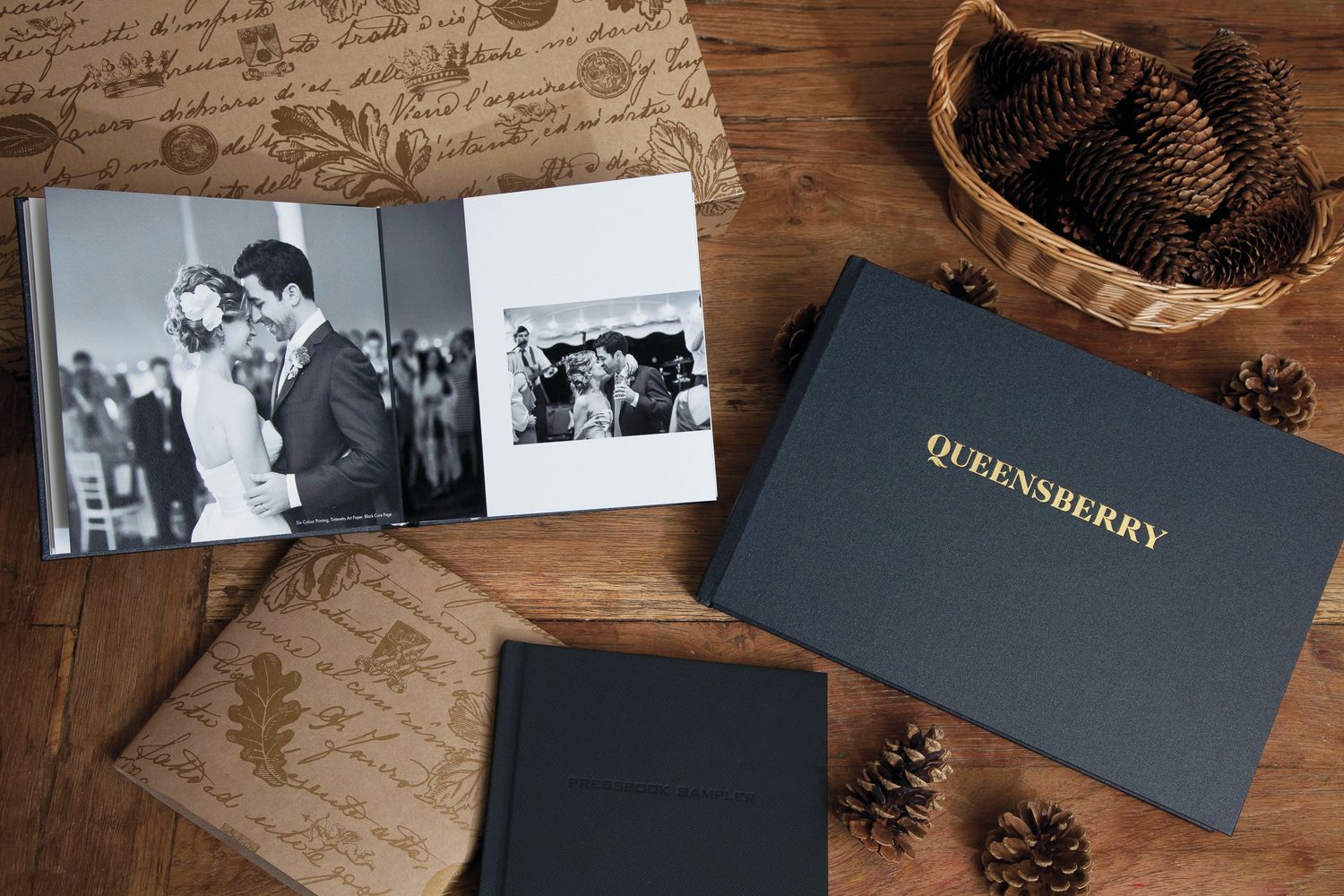 Wedding photo albums and decorative pine cones displayed on weathered wood.