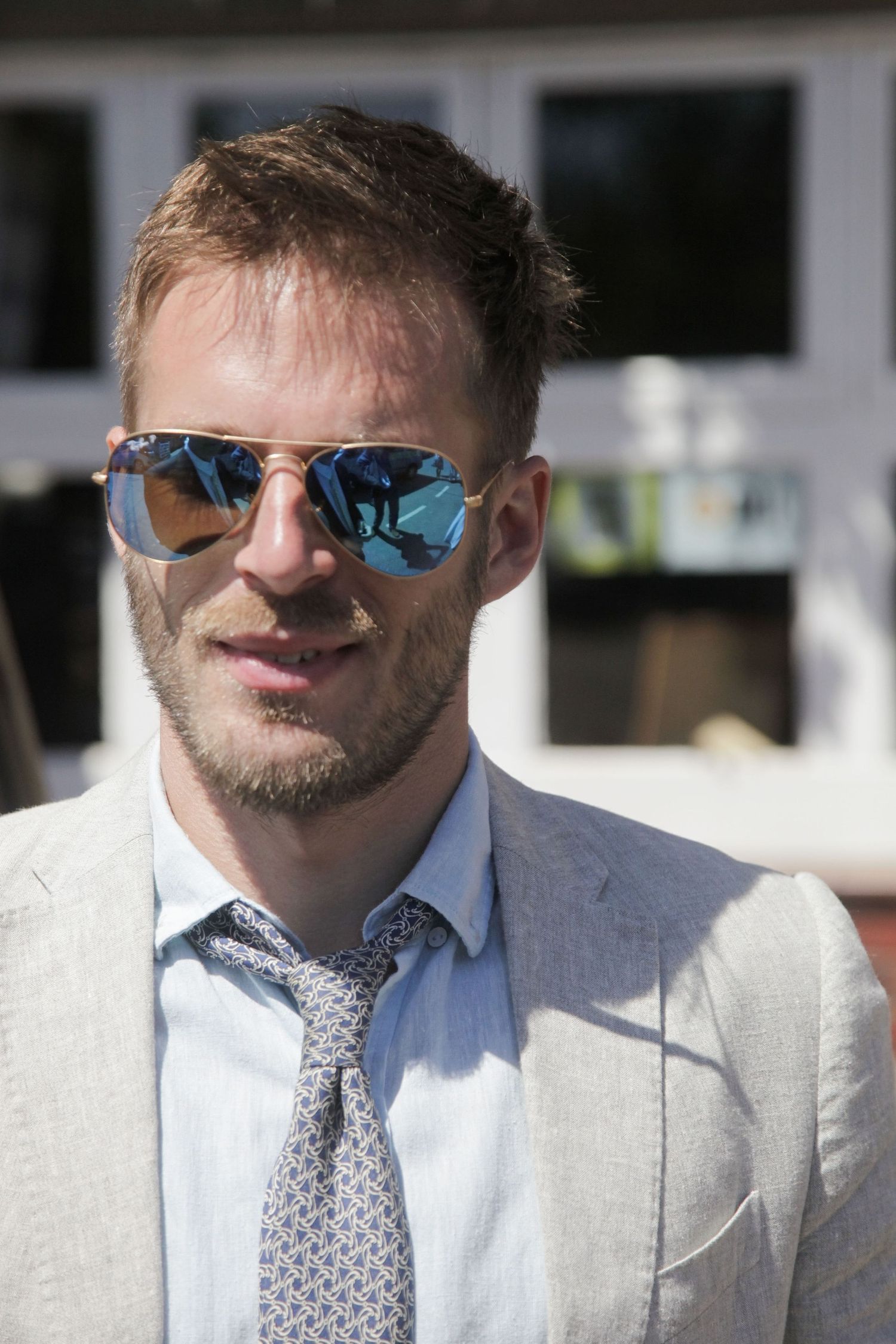Men in light gray suits and patterned ties wearing reflective sunglasses pose outside.