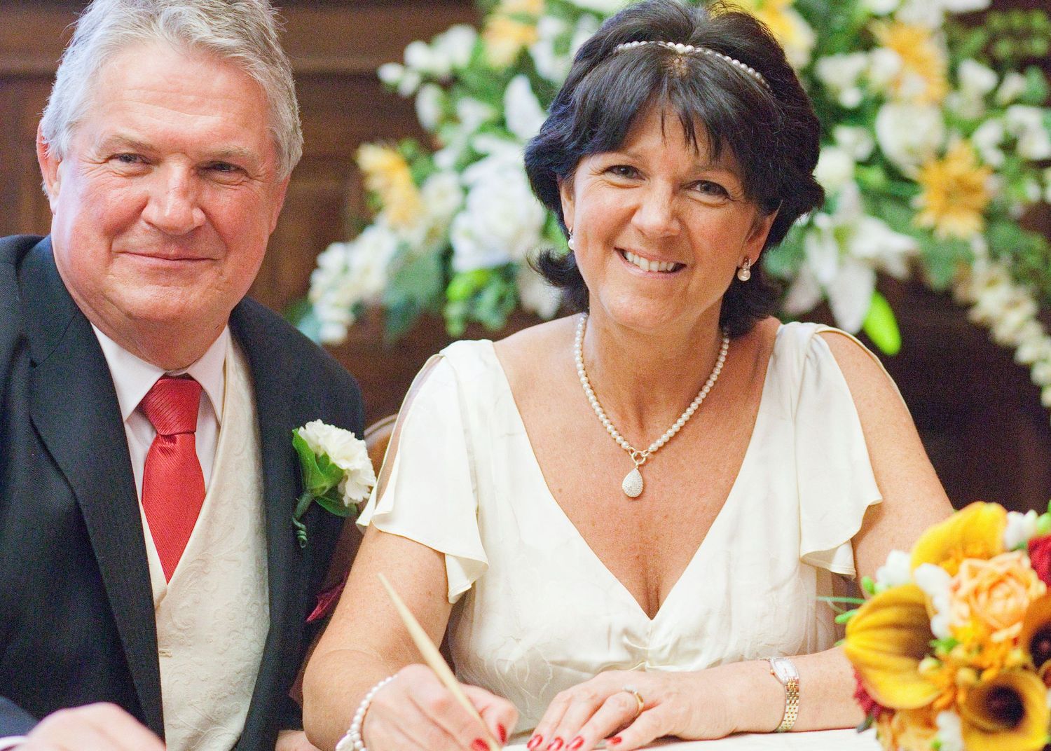 Wedding couple smiling while signing documents with sunflower decorations in elegant venue.
