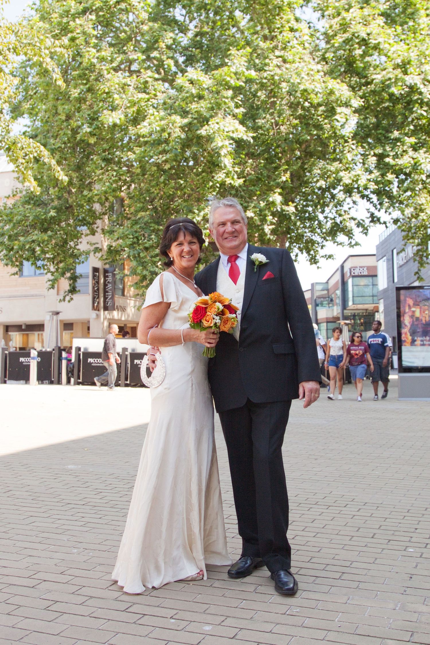 Wedding couple poses on sunny cobblestone street with trees in background.