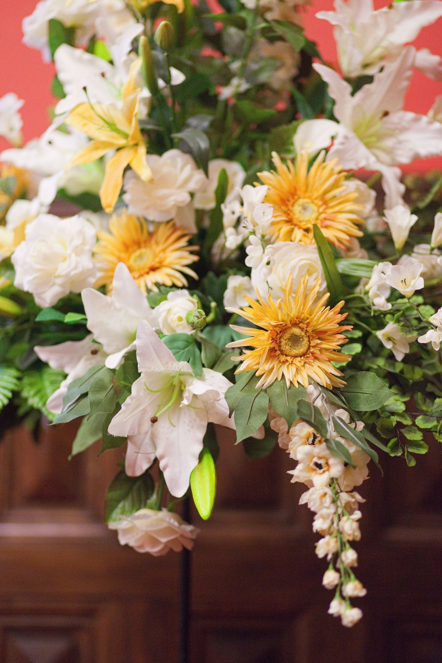 A floral arrangement with white lilies and yellow gerbera daisies against a coral background.