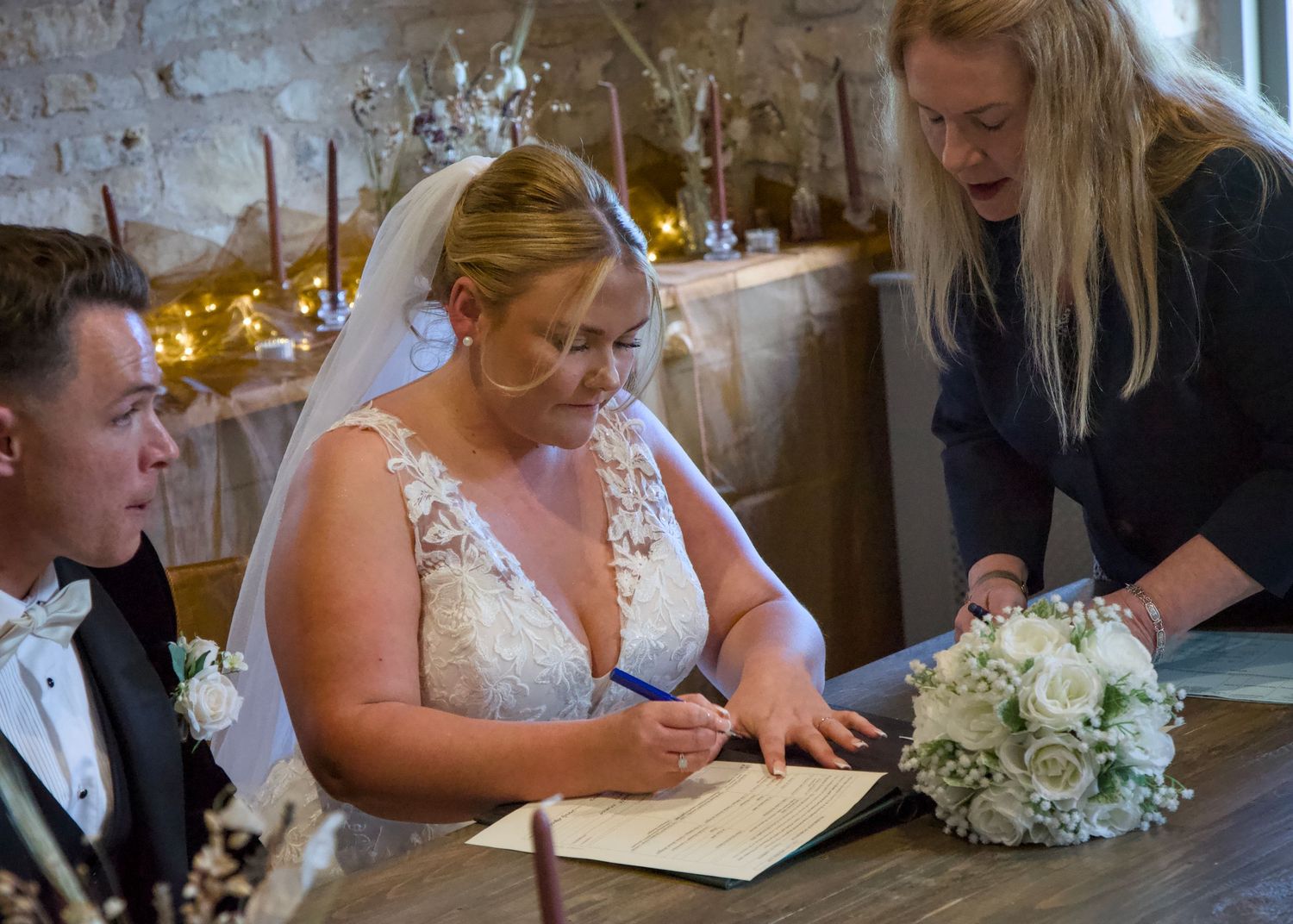 Wedding couple signing official documents during their ceremony with an elegant bouquet nearby.