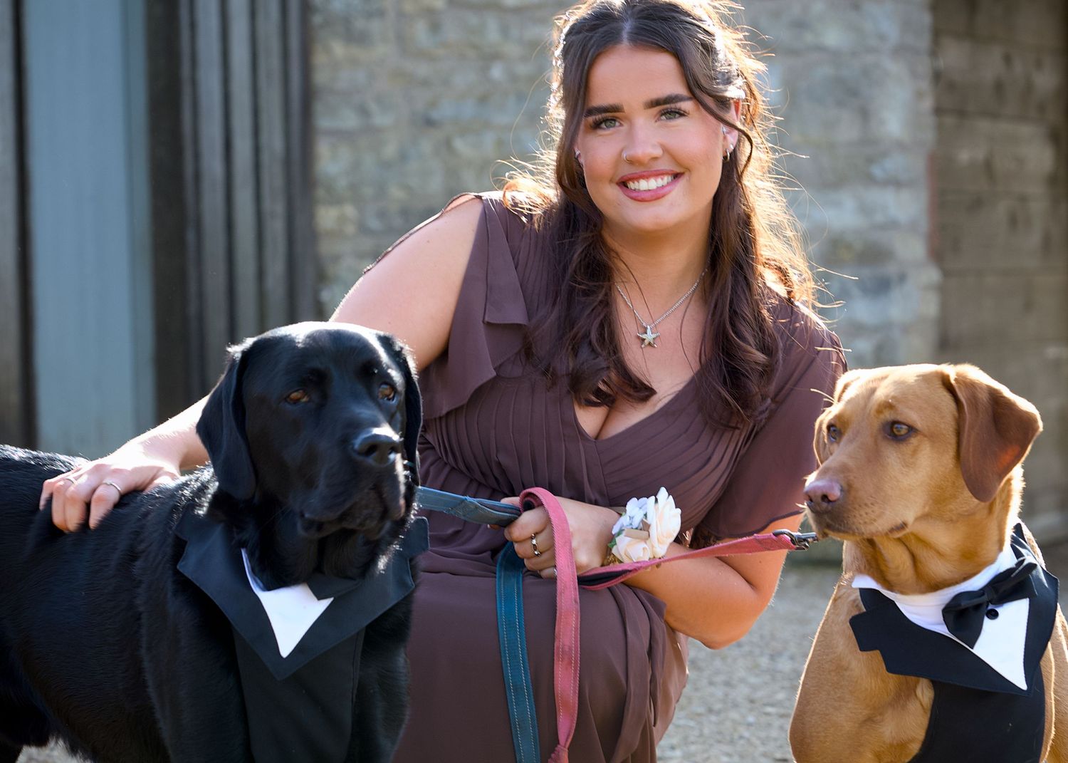 Two dogs wearing formal bow ties pose with their owner outdoors.