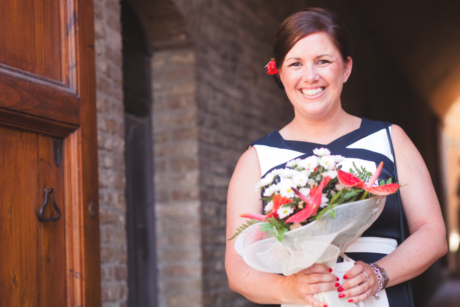 Wedding party members hold bouquets while posing in front of wooden doors.