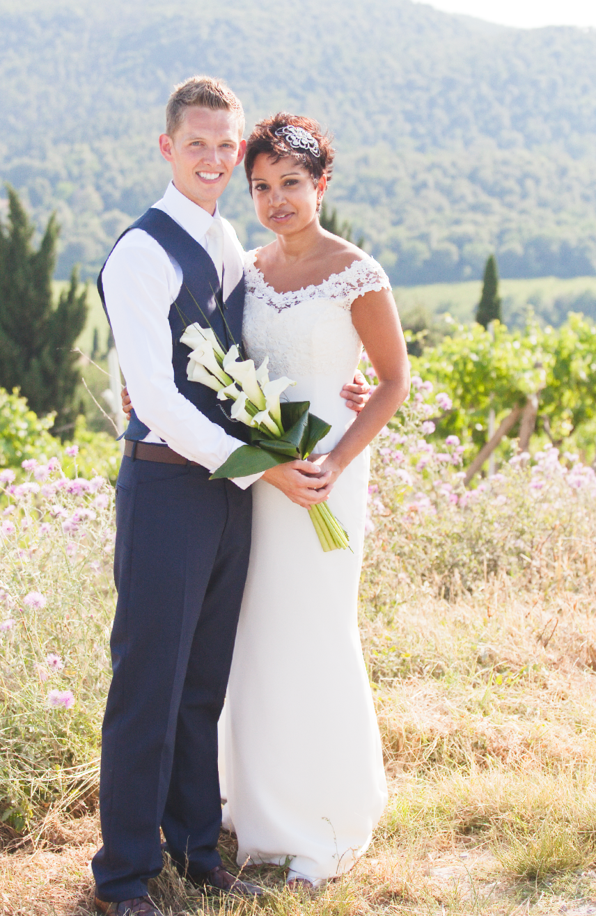 Wedding couple poses in meadow with mountains and wildflowers in background.