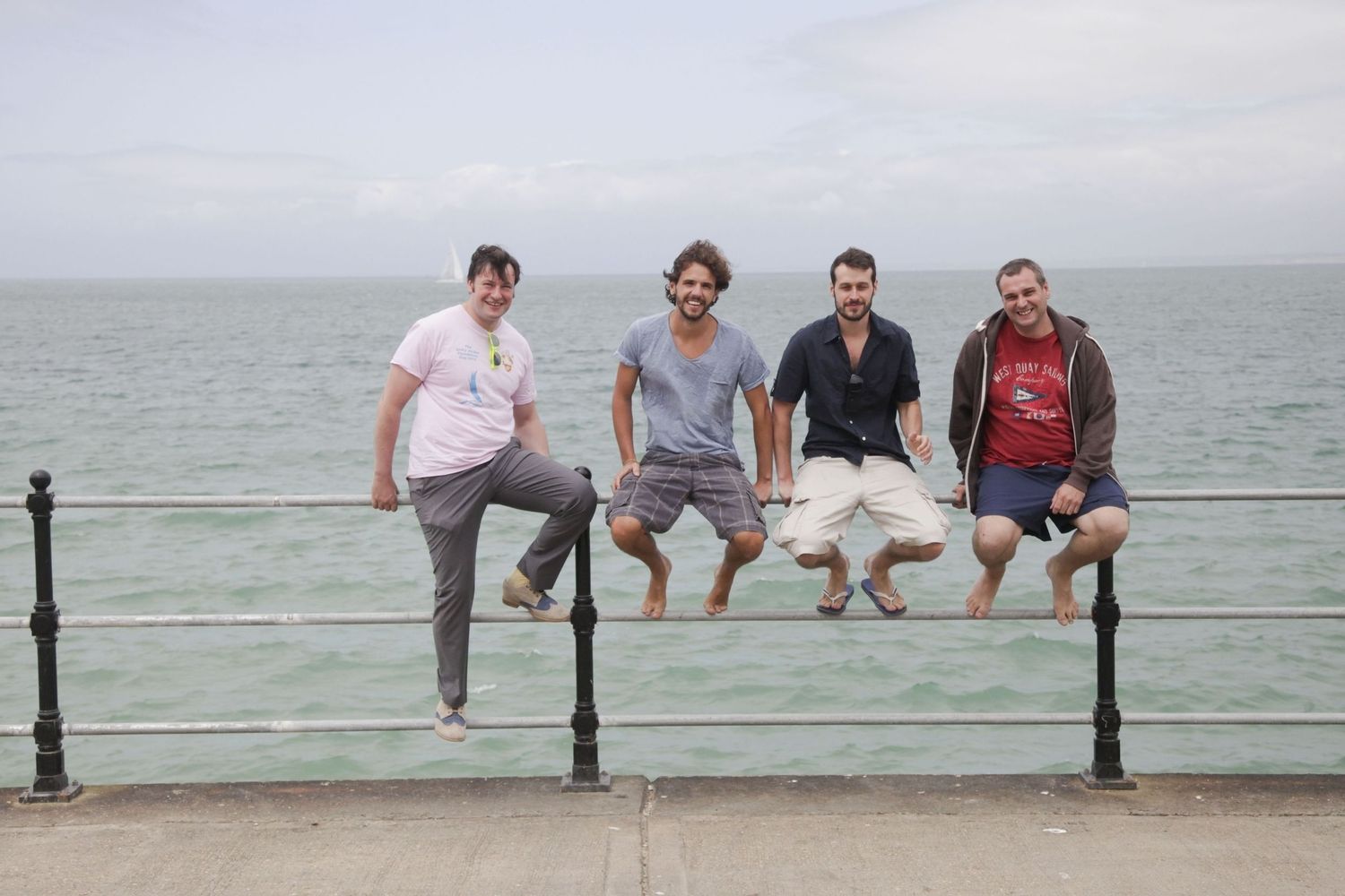 Friends sitting together on a railing overlooking the ocean on a cloudy day.