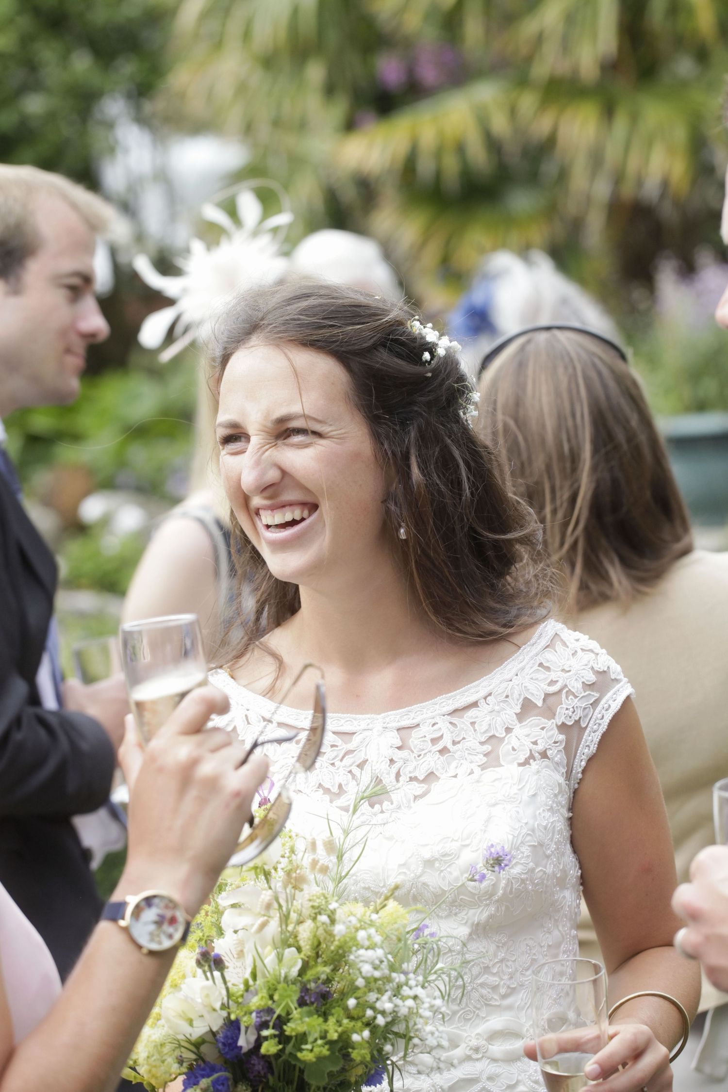 Bride in lace dress laughs joyfully during outdoor garden reception.