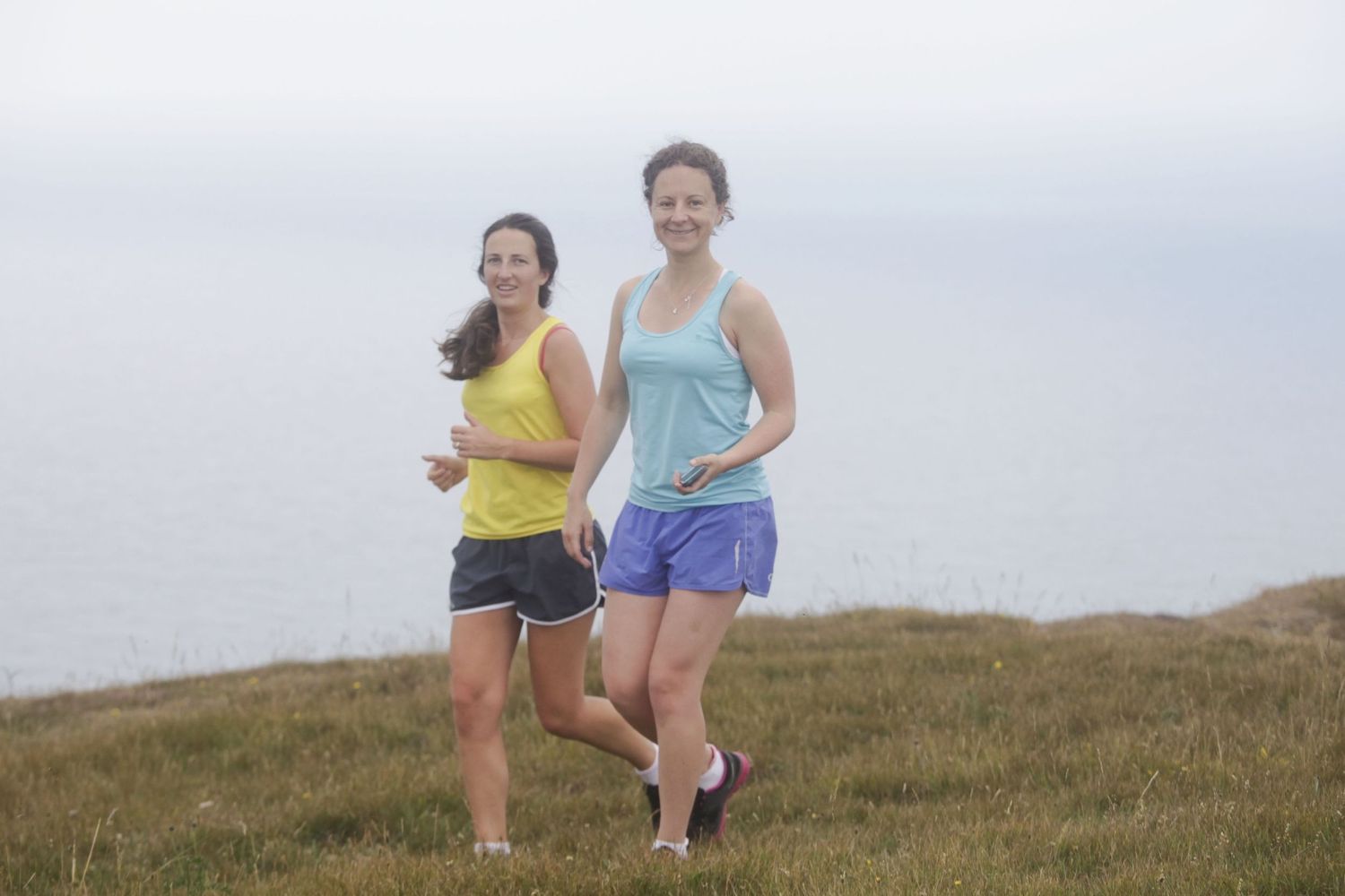 People sitting and posing together on a grassy hillside overlooking a scenic view.