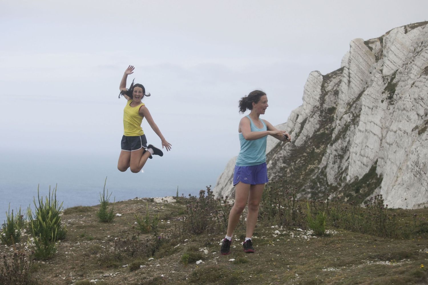 People jumping and posing on grassy cliffs overlooking the ocean.