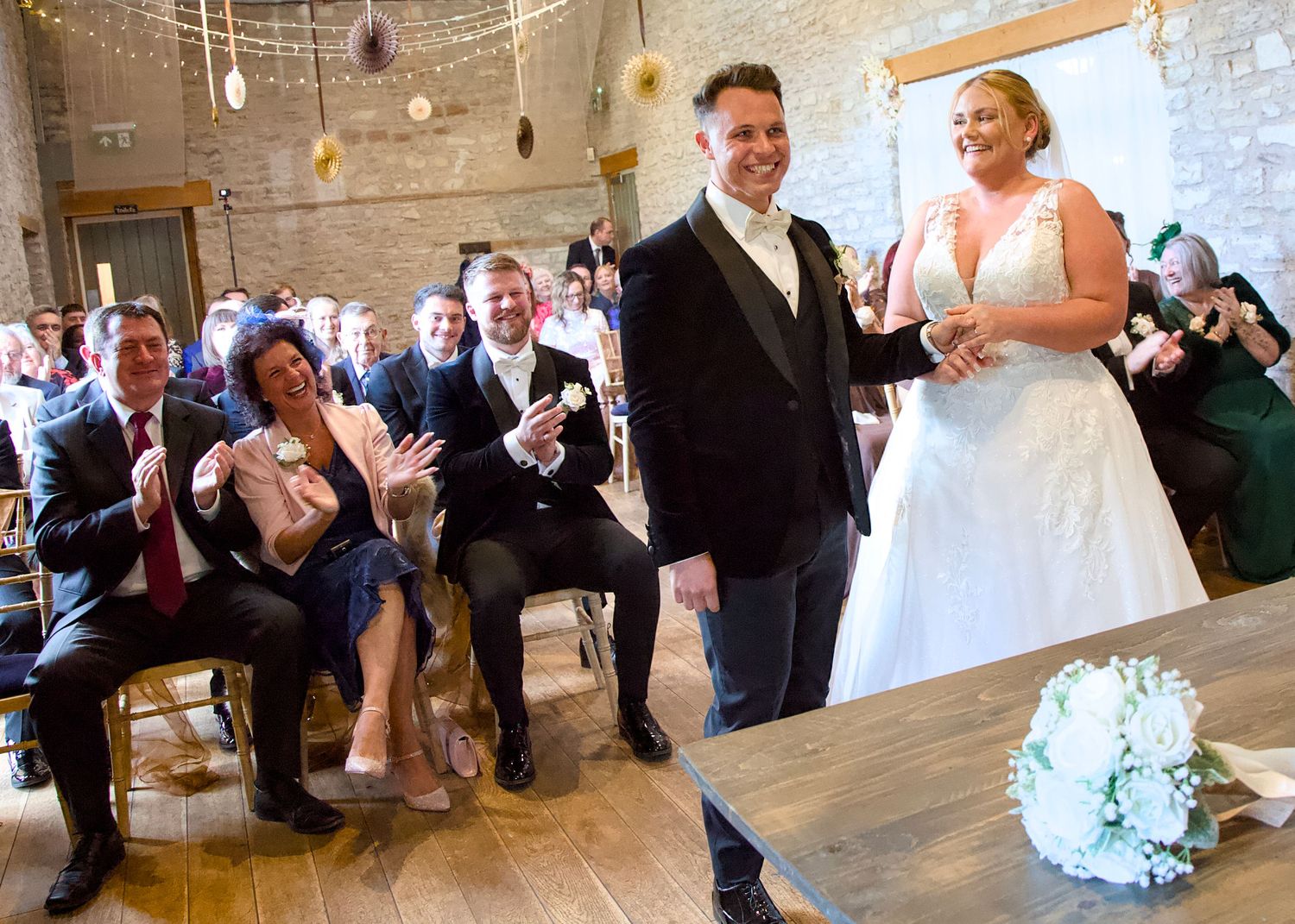 Wedding guests dancing and celebrating on a rustic wood floor during a reception.