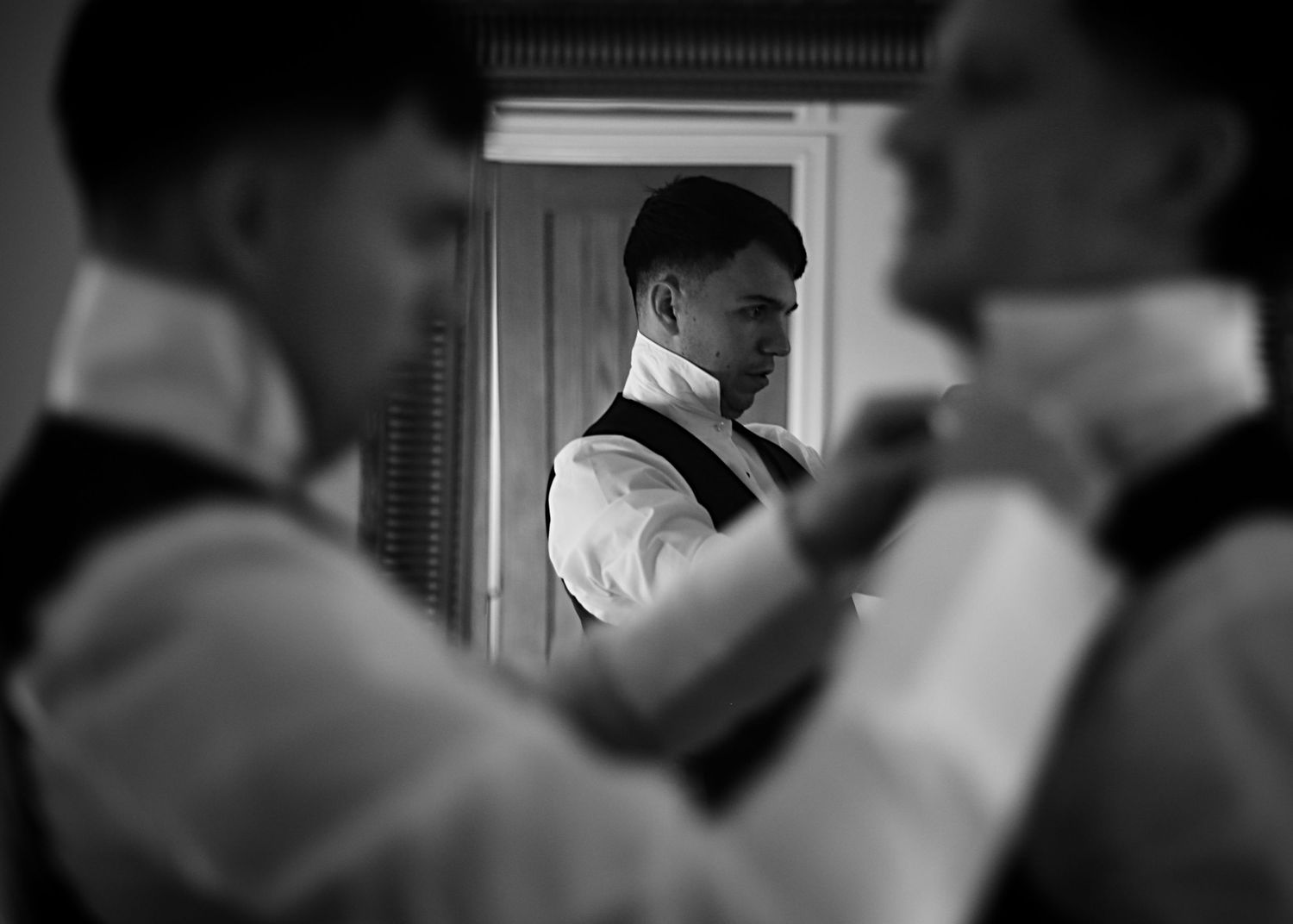 A moody black and white image of wedding preparations reflected in mirrors.
