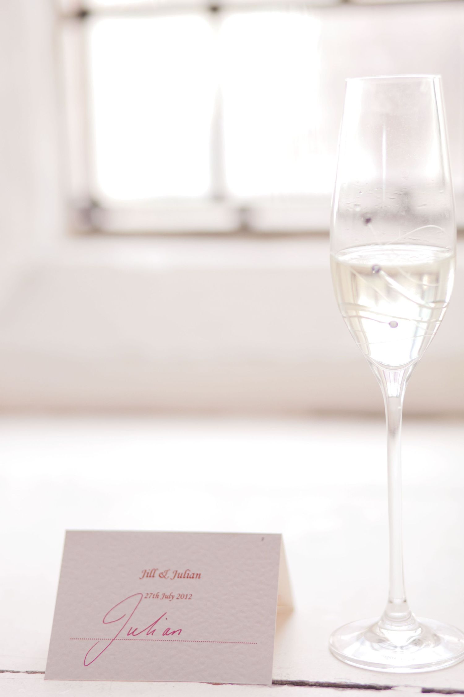 Place cards and champagne glasses arranged on a white tablecloth in natural window light.