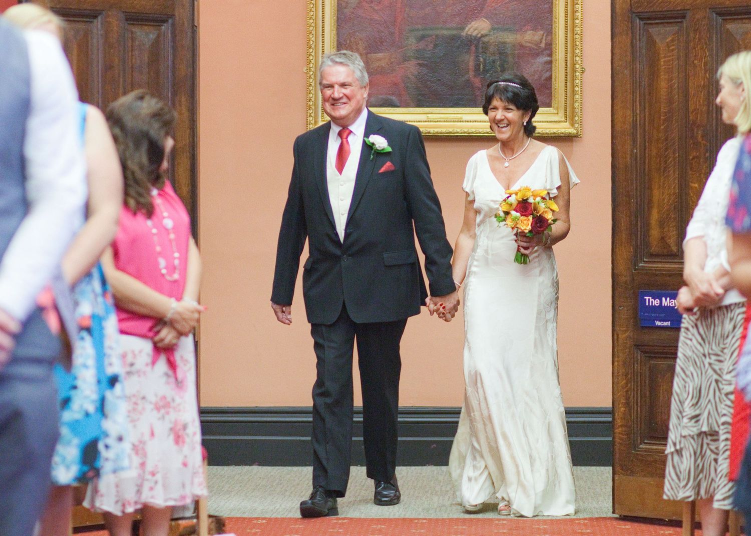 Wedding guests walk through an elegant hallway with wooden doors and coral walls.
