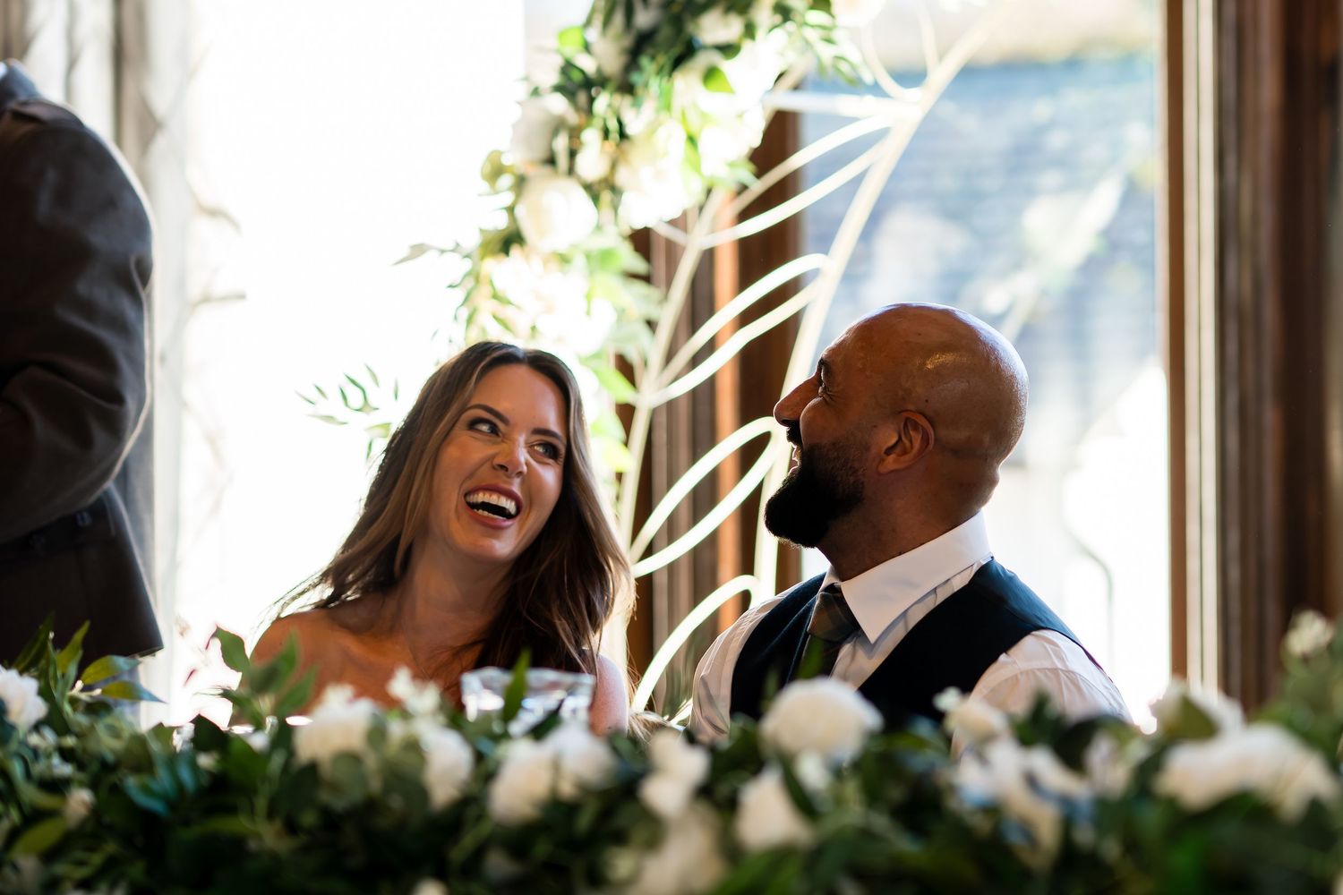A couple shares a joyful moment while sitting together in natural window light.