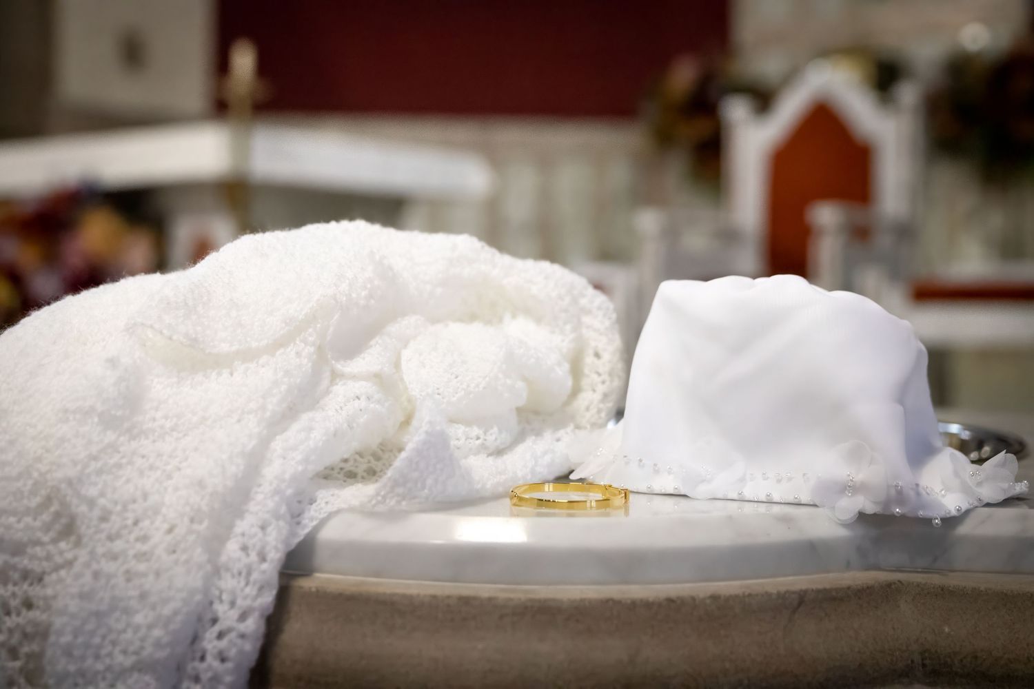 White baptism gown and bonnet with gold rings on a church font, symbolizing a Catholic baptism ceremony.