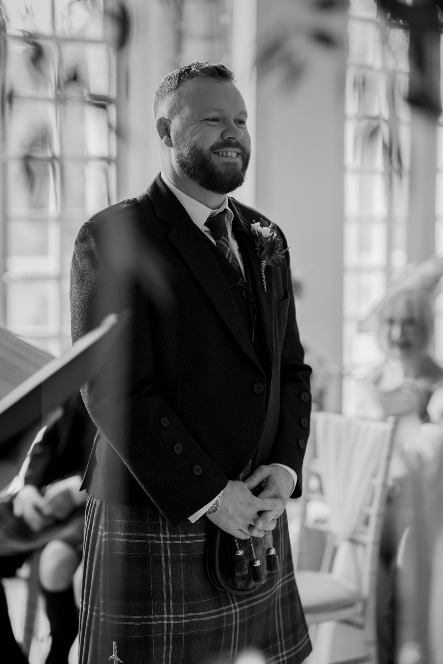 Smiling groom in traditional Scottish kilt and jacket stands at the altar during a wedding ceremony.