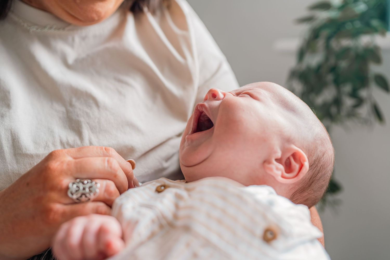 A newborn baby yawning while being cradled in a mother's arms, wearing a white knit outfit.