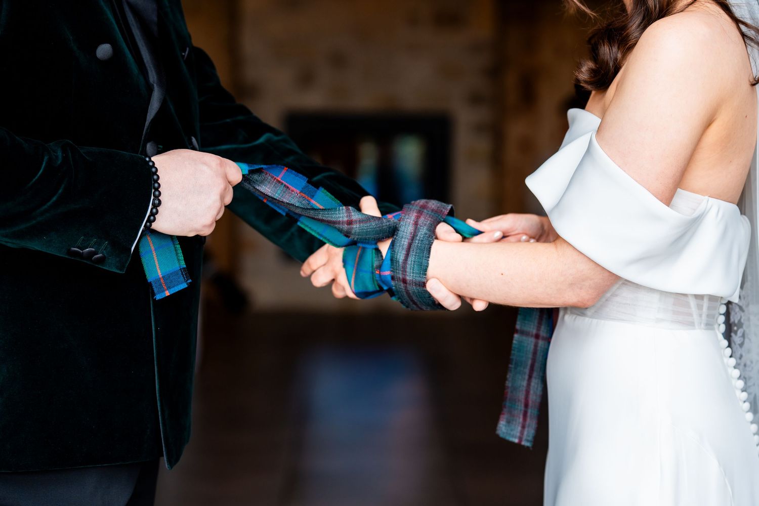 Couple performing a handfasting ceremony with a blue tartan ribbon during their wedding.