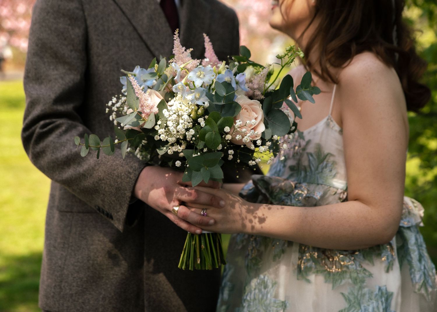 Close-up of a delicate pastel wedding bouquet with blue and pink flowers being held by a couple.