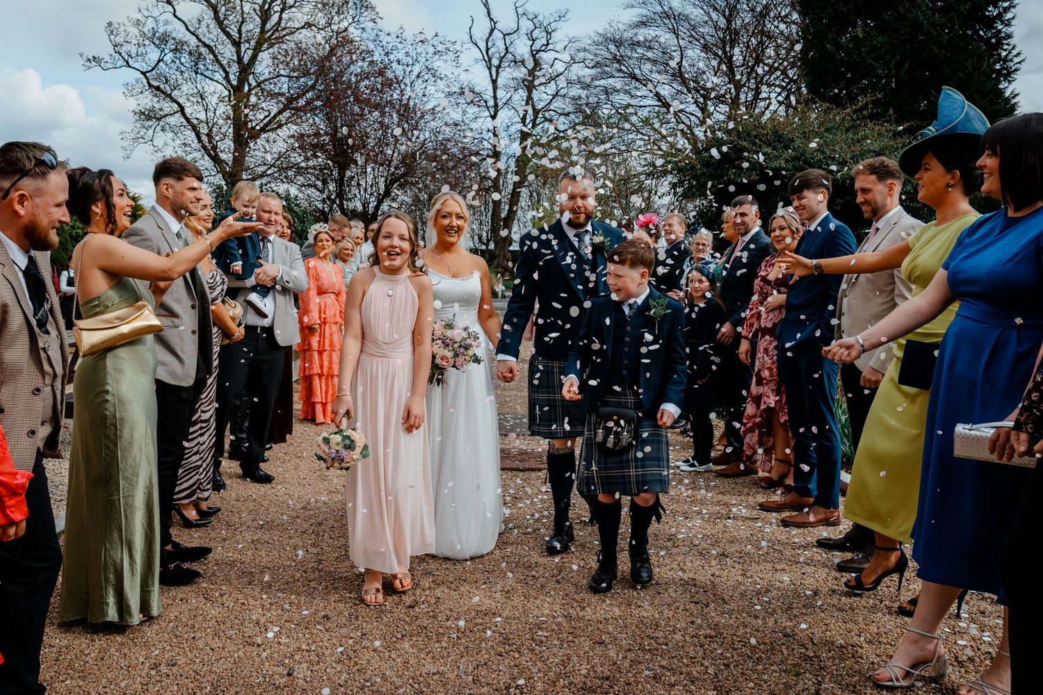 Wedding couple walks through confetti shower with bridal party and guests celebrating outdoors at a Scottish wedding.