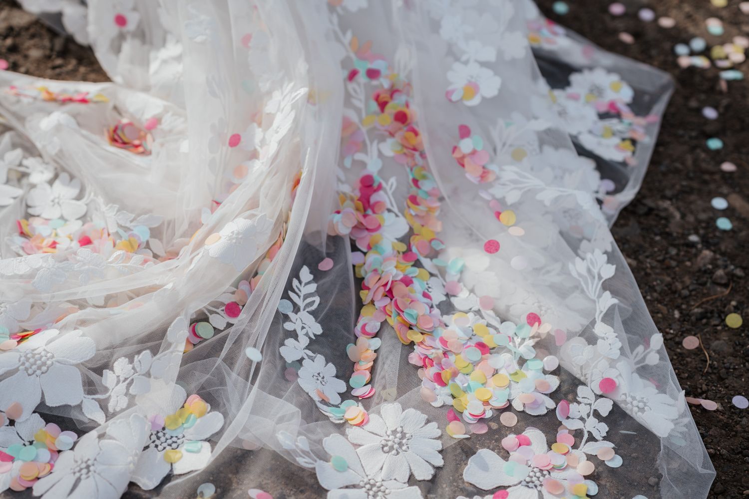 White floral tulle fabric with colorful confetti scattered across delicate embroidered flowers.