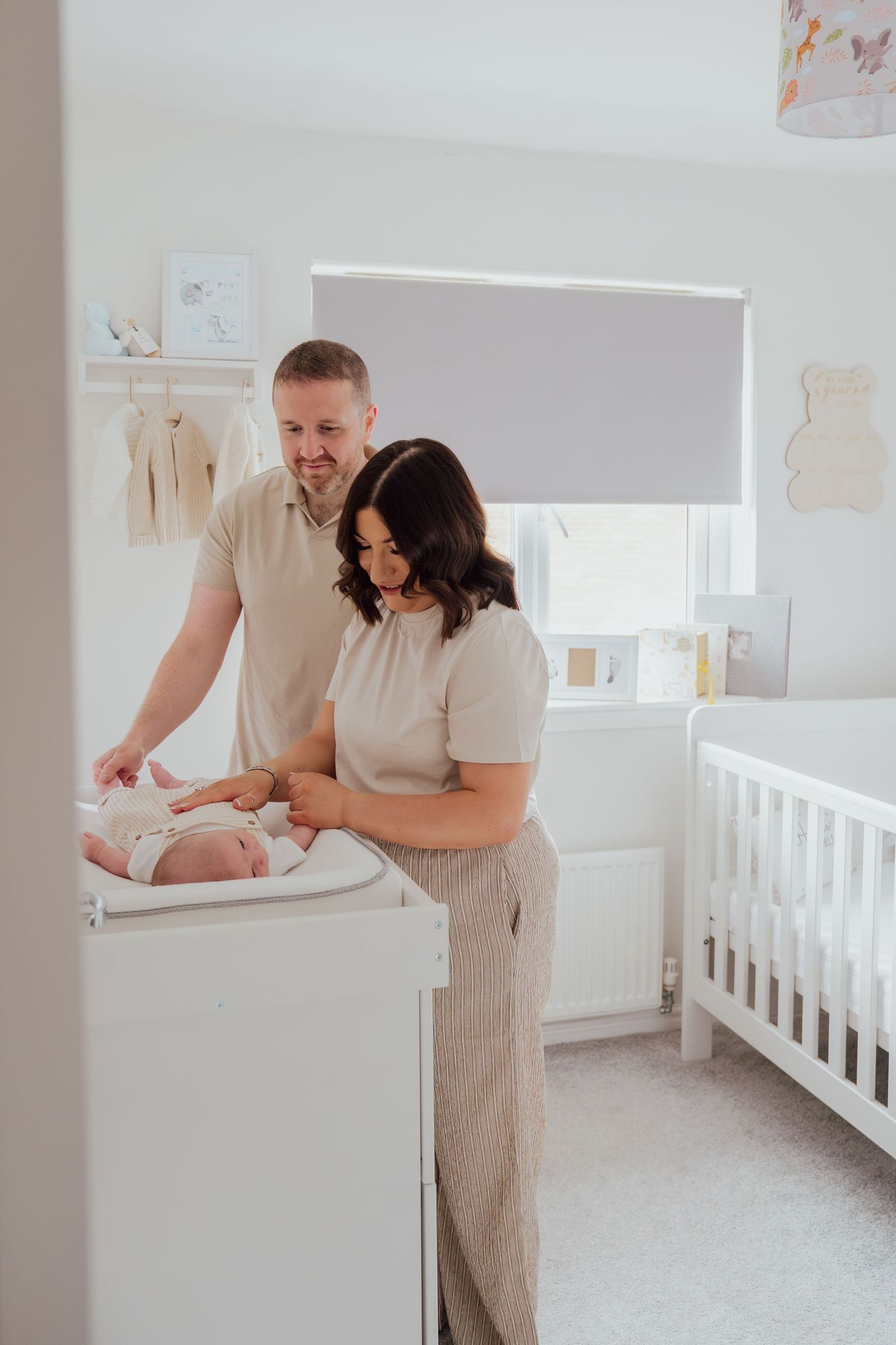 New parents smiling over their newborn baby on a changing table in a bright white nursery room.