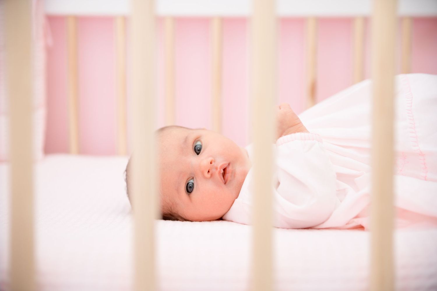 Newborn baby resting peacefully in pink crib with soft lighting.