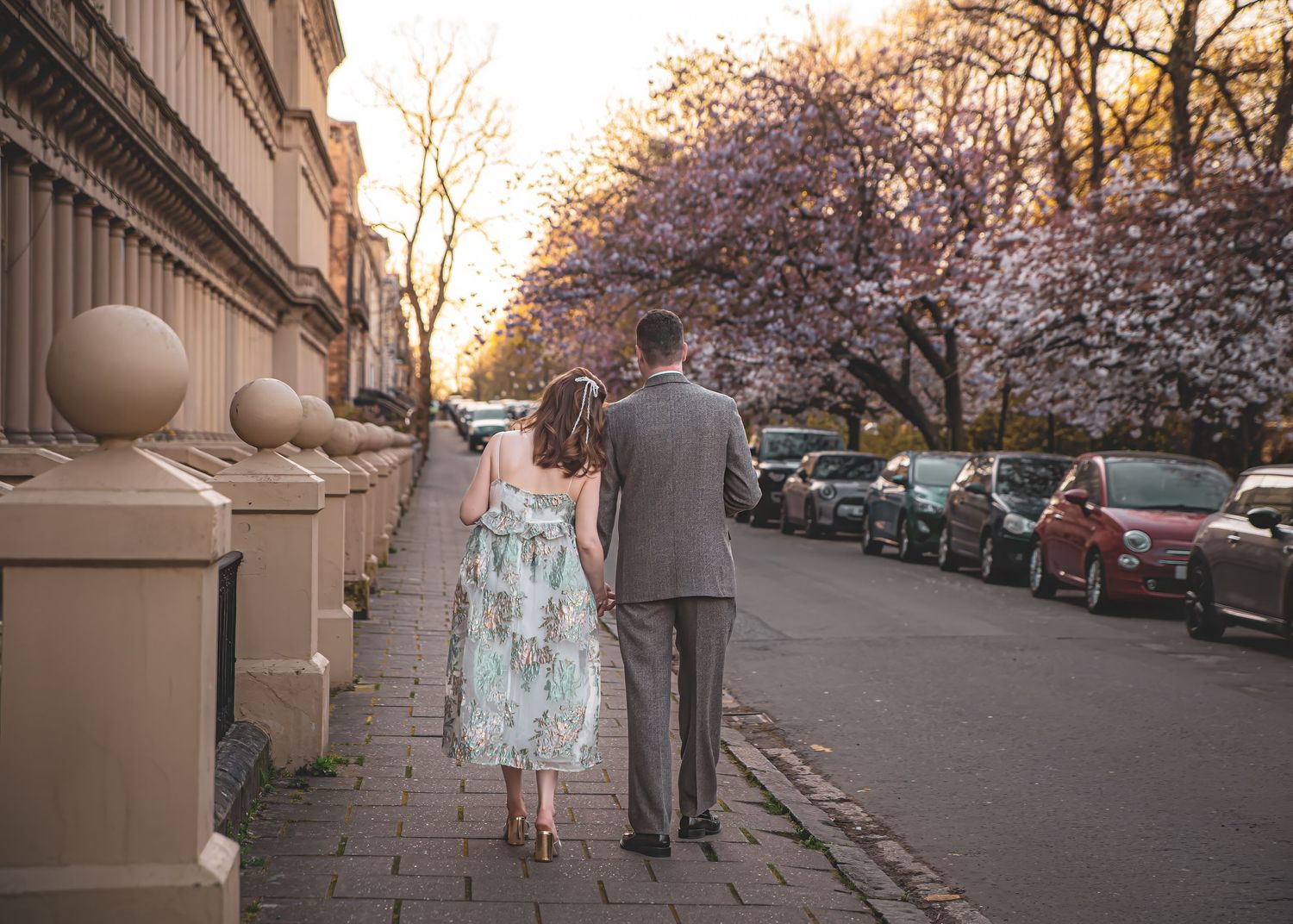 A couple walking hand in hand down a street lined with blooming cherry trees.