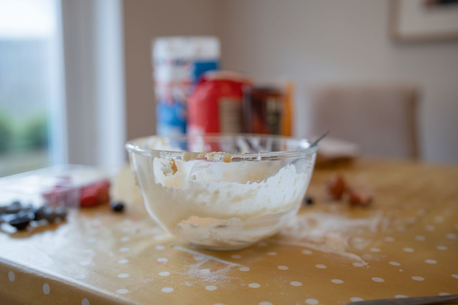 Glass bowl of whipped cream on a polka dot tablecloth with baking ingredients in the background.