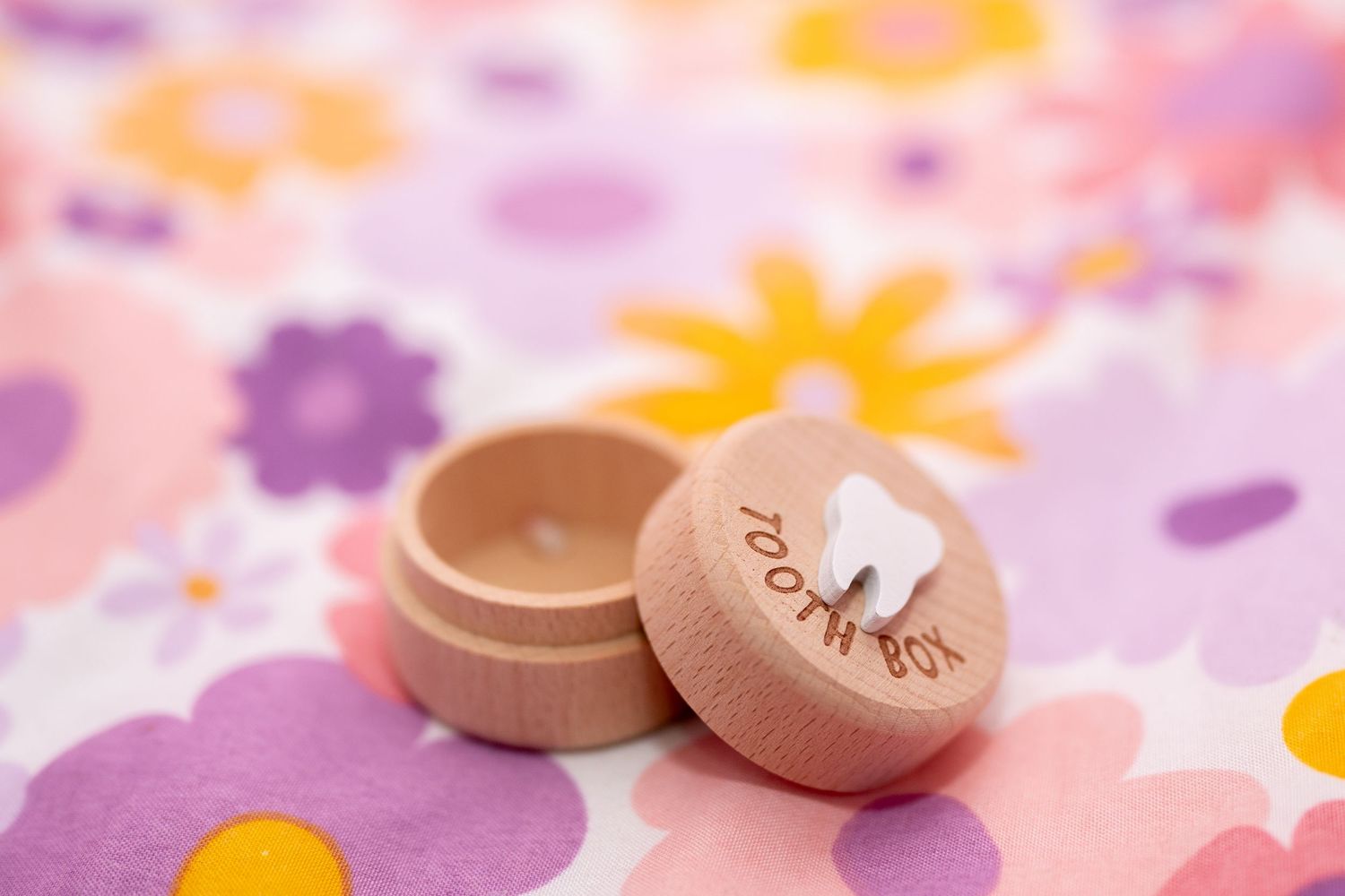 Wooden tooth fairy box with engraved tooth design on floral pink background for baby first lost tooth keepsake.