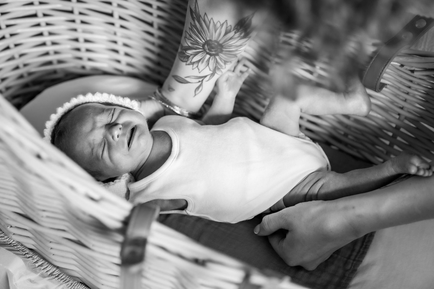 Black and white photo of a newborn baby lying in a wicker bassinet, swaddled in a white onesie.
