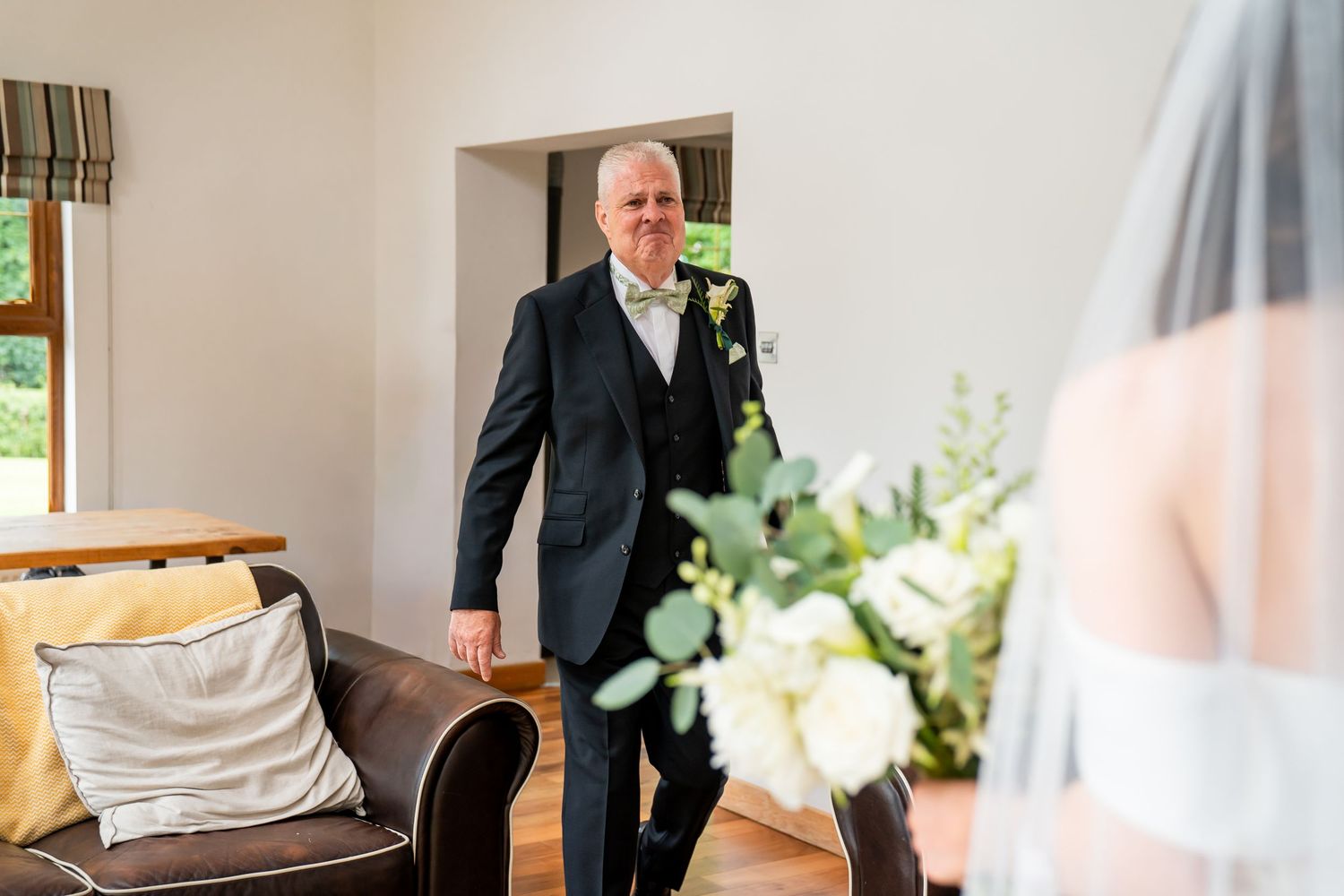 Father of the bride smiling as he sees his daughter in her wedding dress and veil for the first time.
