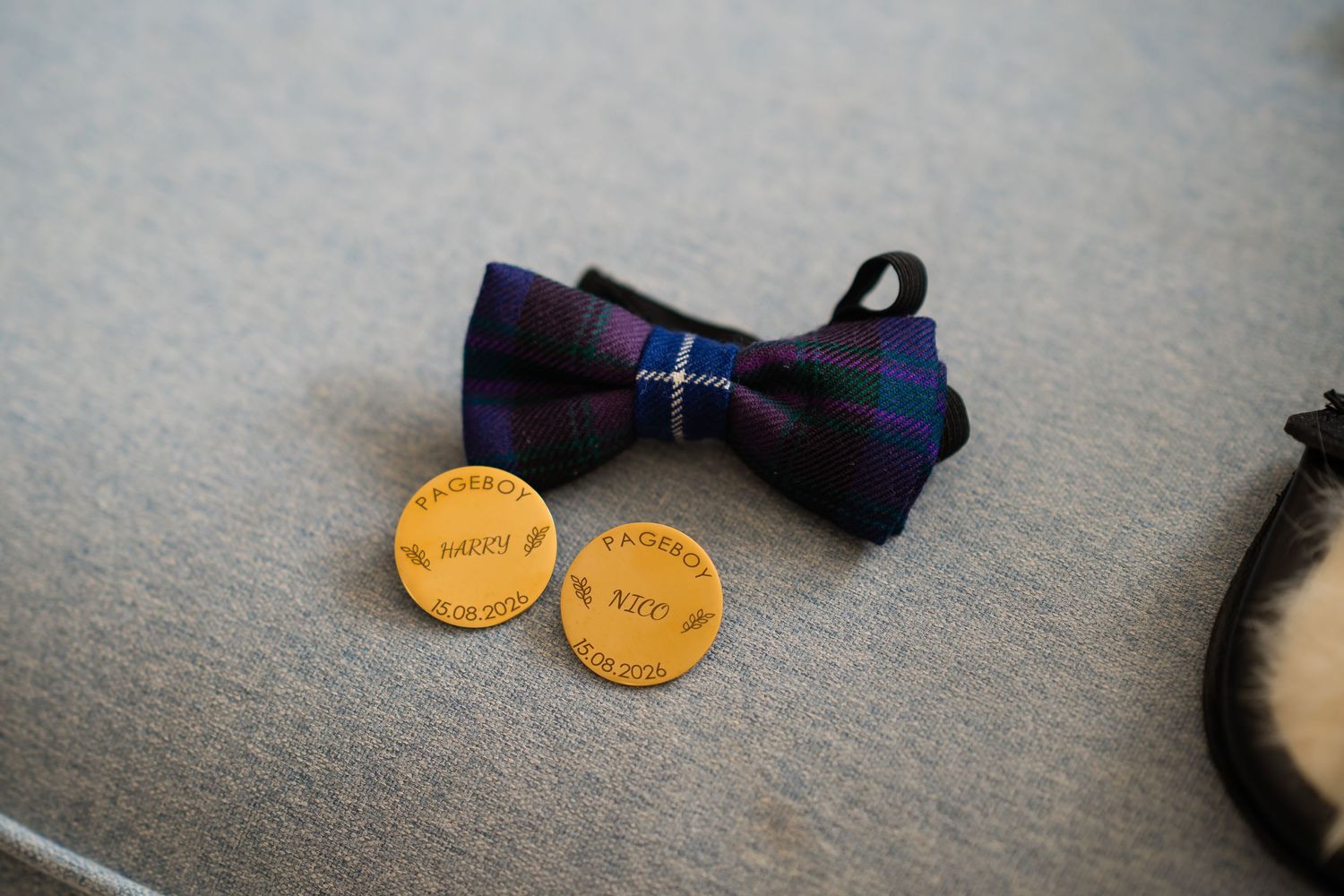 Navy tartan bow tie with engraved wooden cufflinks on gray surface, elegant wedding accessories.