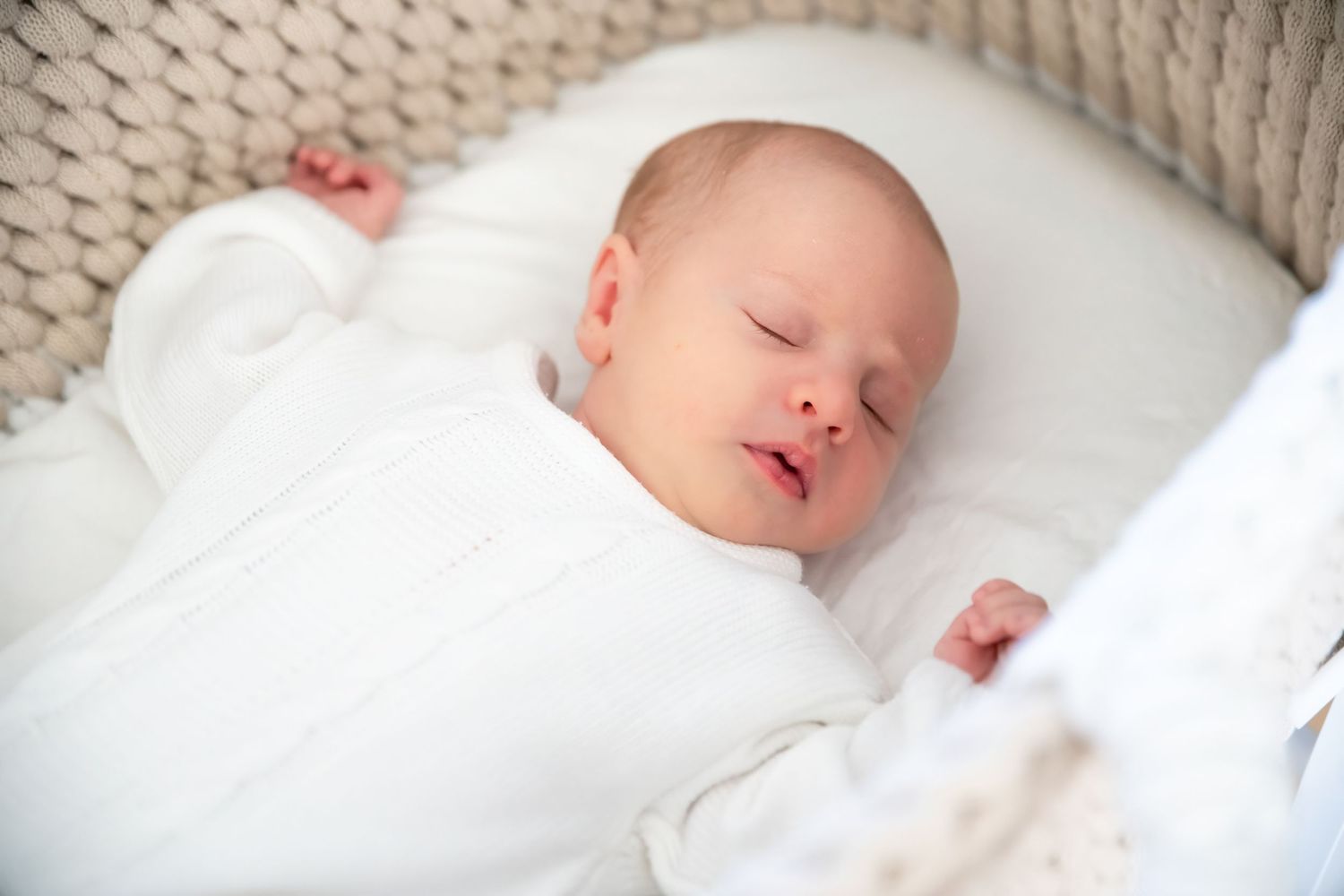 Sleeping newborn in white bassinet with woven details.