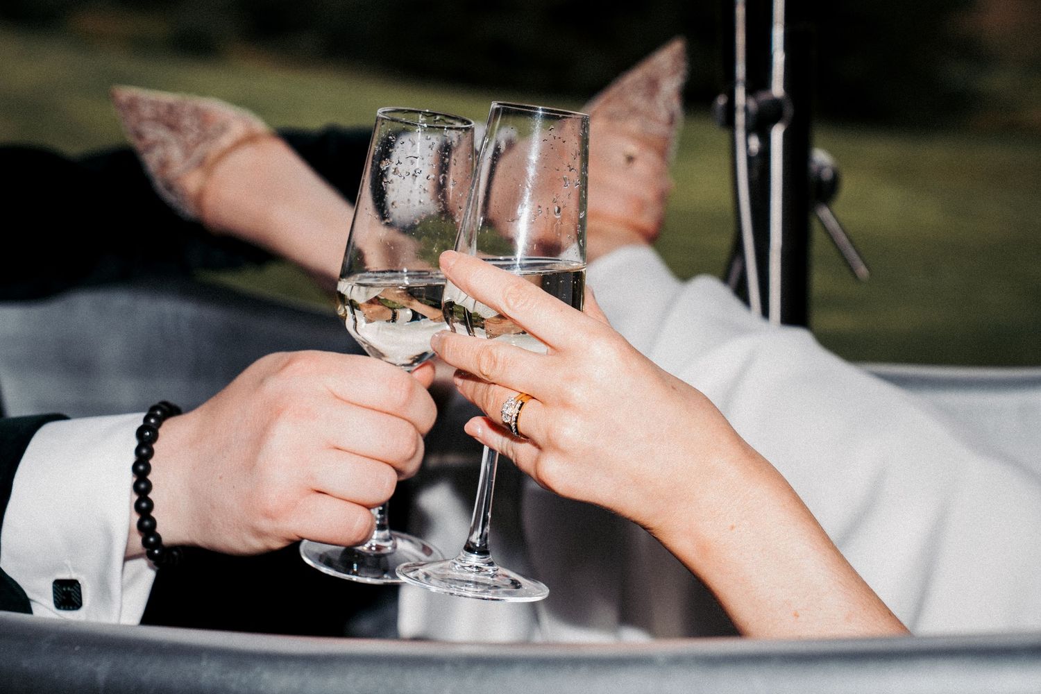 Two people clinking champagne glasses in a wedding toast, showcasing elegant rings and a beaded bracelet.