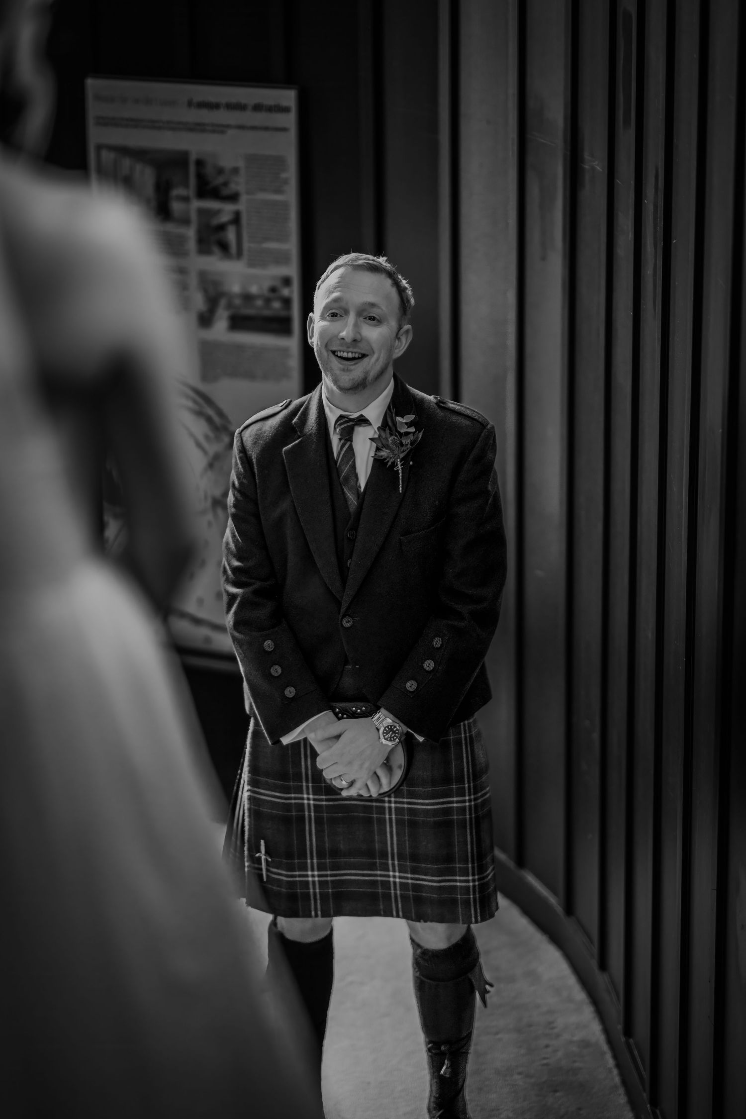 Smiling groom in traditional Scottish kilt and jacket at wedding ceremony, black and white photo.