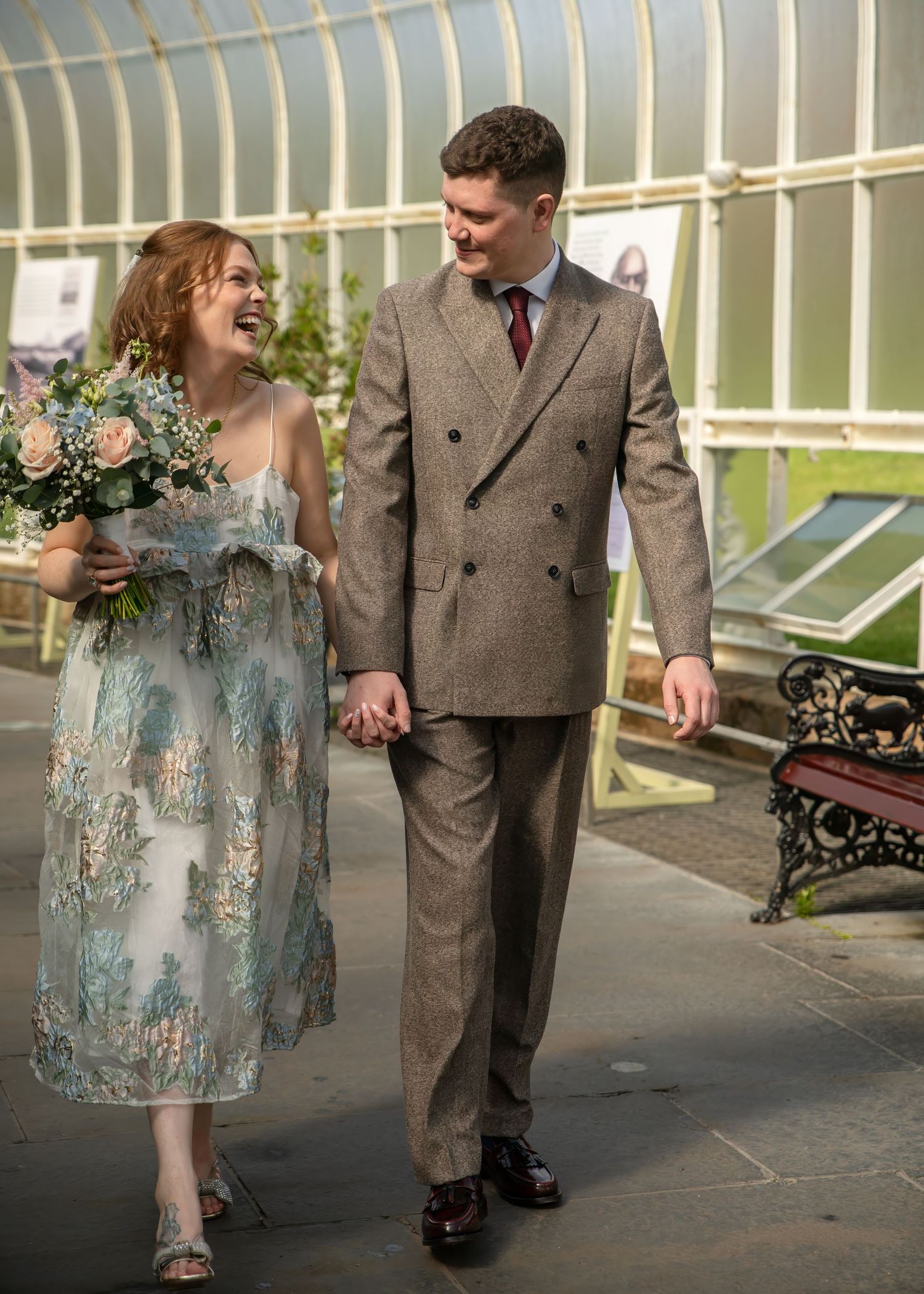 Couple in vintage attire walking through conservatory garden setting.