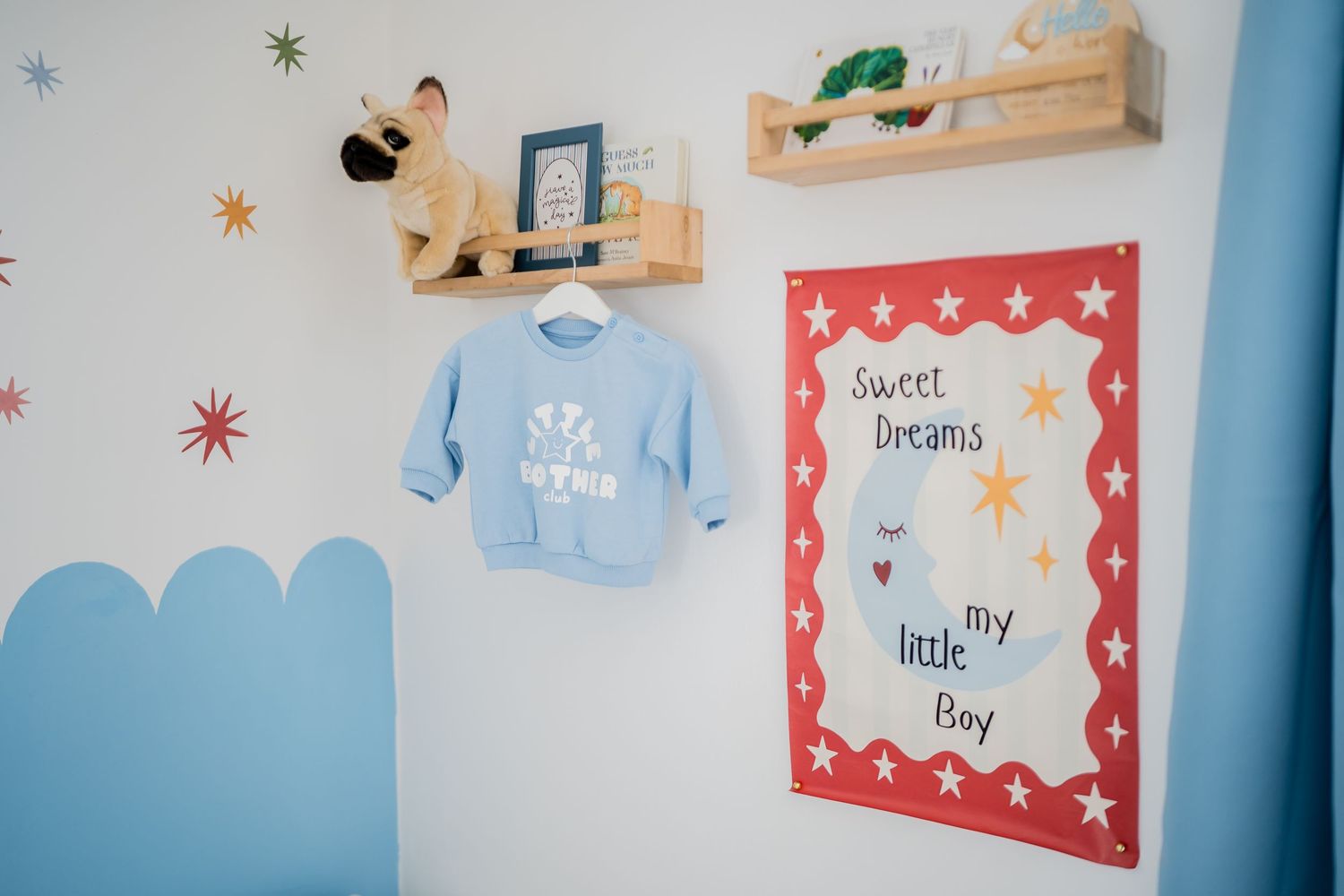 Baby boy nursery wall decor featuring a blue sweater, wooden shelves, star accents, and a Sweet Dreams poster.