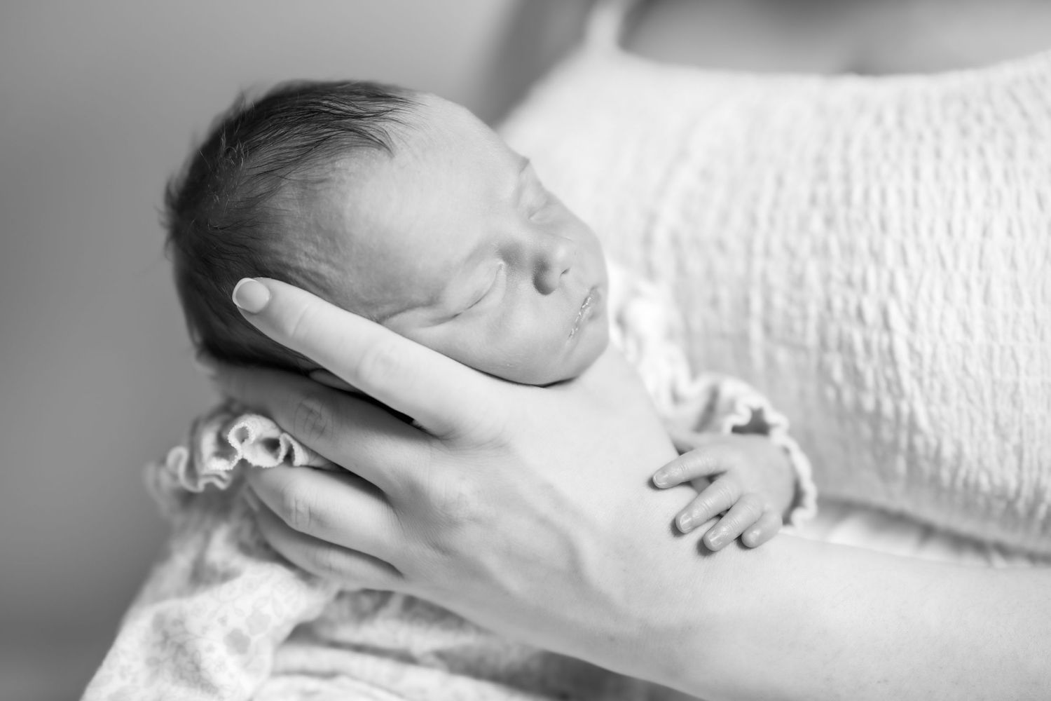 Black and white photo of a sleeping newborn baby cradled gently in an adult's hand.