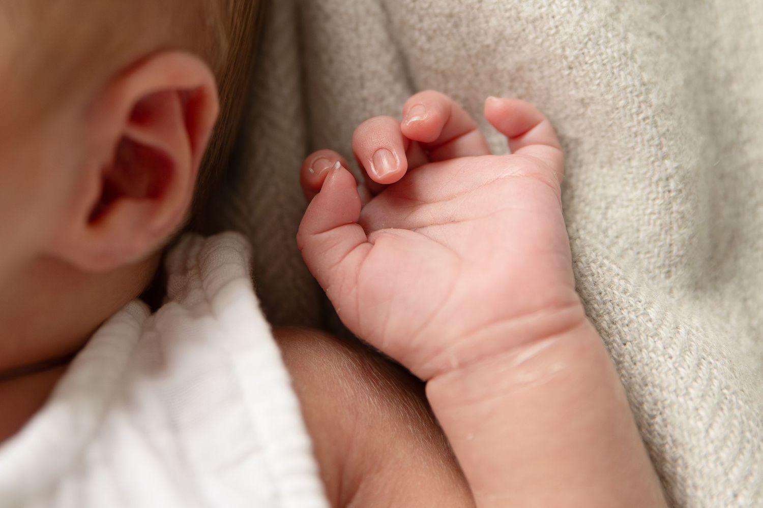 Close-up of tiny baby hand grasping soft fabric.