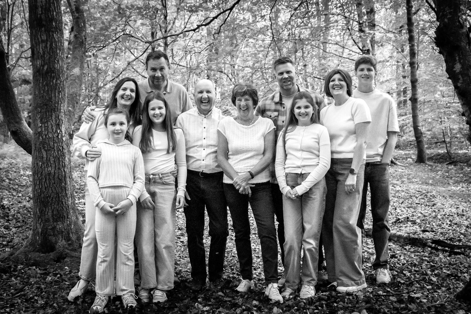 Extended family portrait in casual attire gathered in wooded setting.