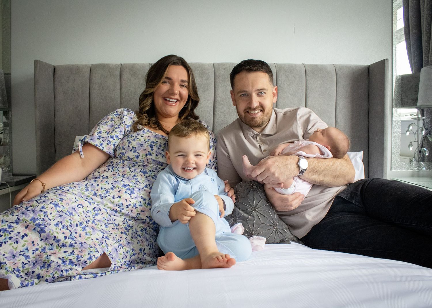 Family lounging together on a bed sharing playful moments in a bright bedroom.