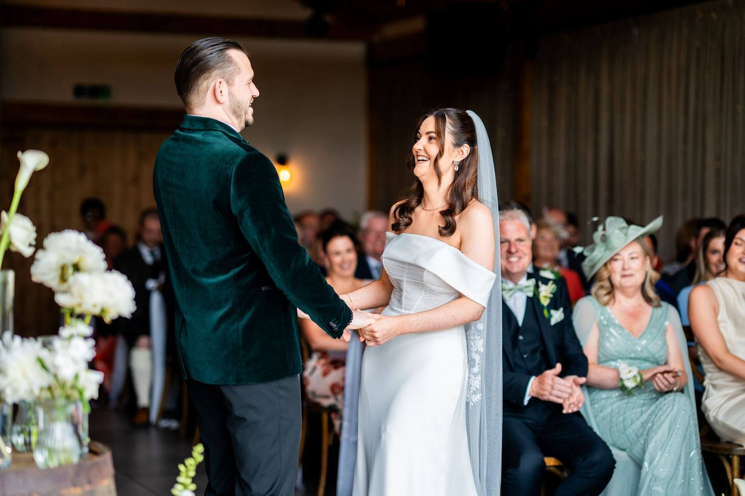Bride and groom share a joyful moment at their wedding ceremony, guests smiling in background.