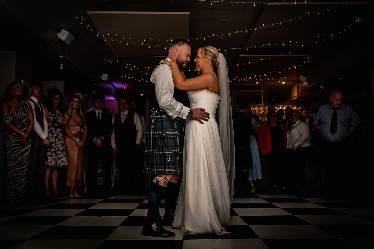 Bride and groom share first dance on black and white checkered floor at romantic wedding reception.