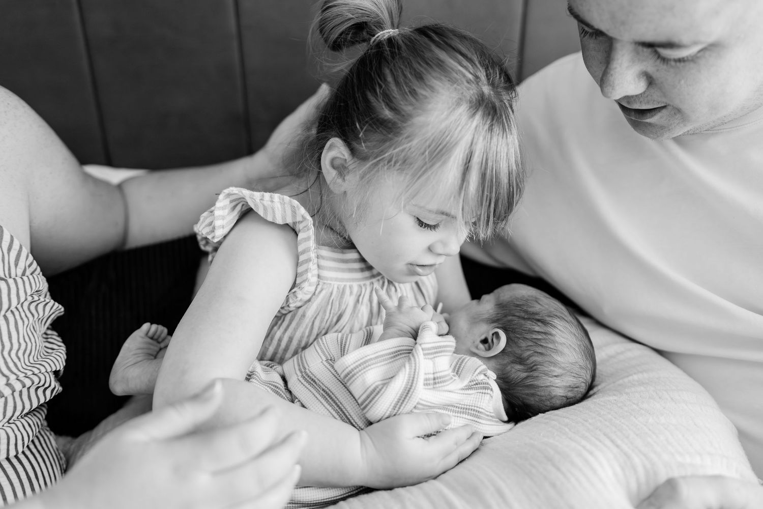 Black and white photo of a young girl tenderly holding a newborn baby while mother watches lovingly nearby.