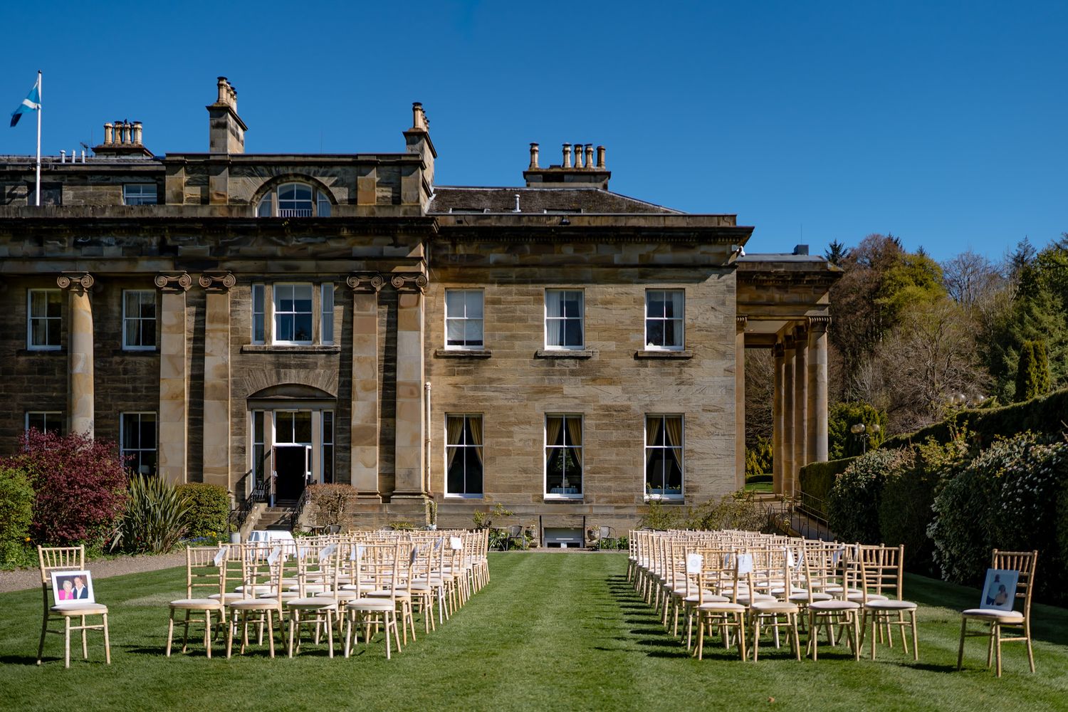 Elegant outdoor wedding ceremony setup with gold chairs on manicured lawn of a grand Georgian country house estate.