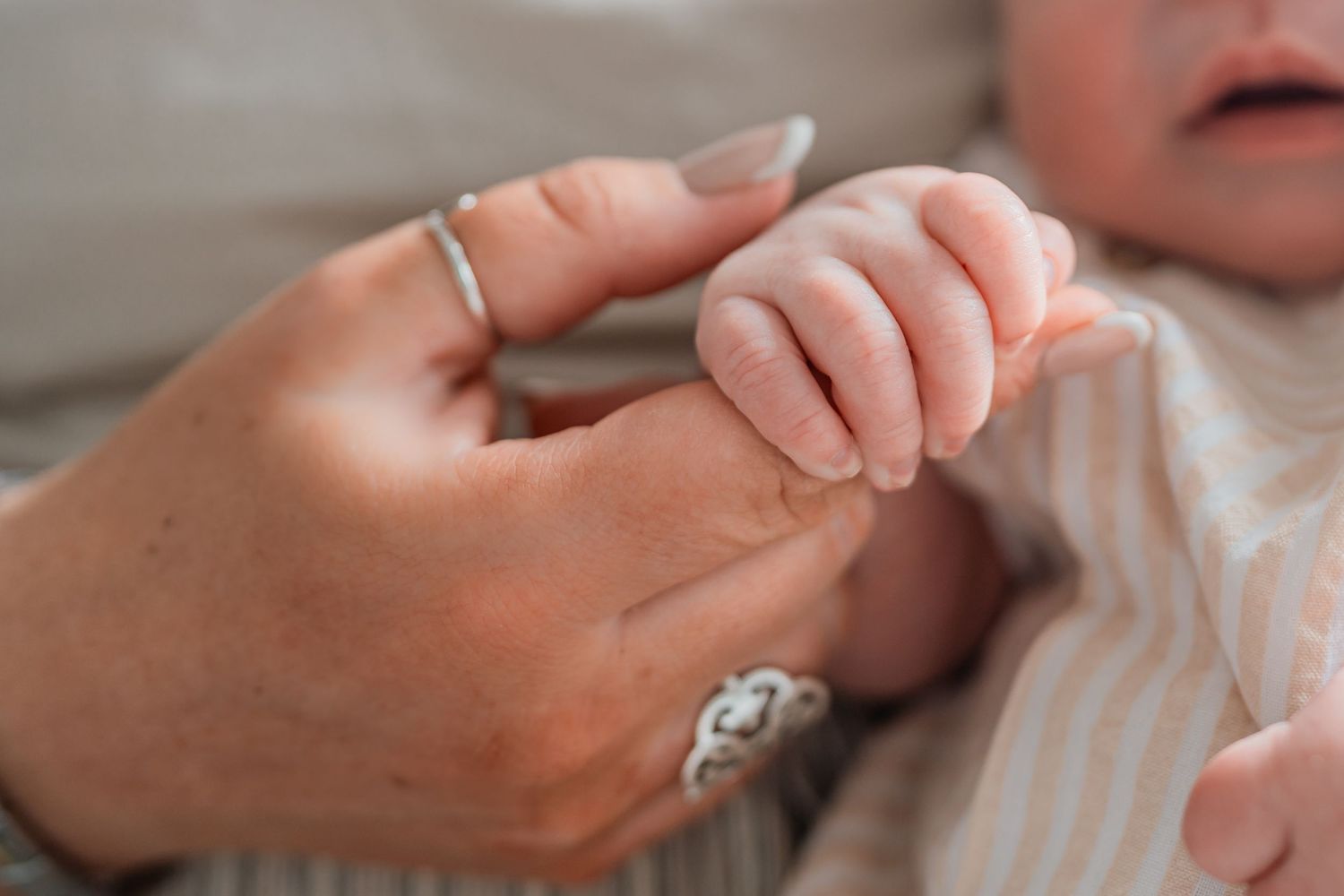 Newborn baby grasping mothers finger, close-up of tiny infant hand holding adult finger, bonding moment.