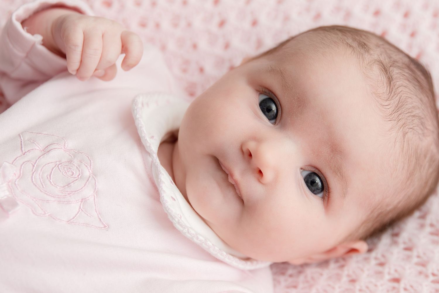 Close-up portrait series of a baby on pink bedding with delicate lighting.