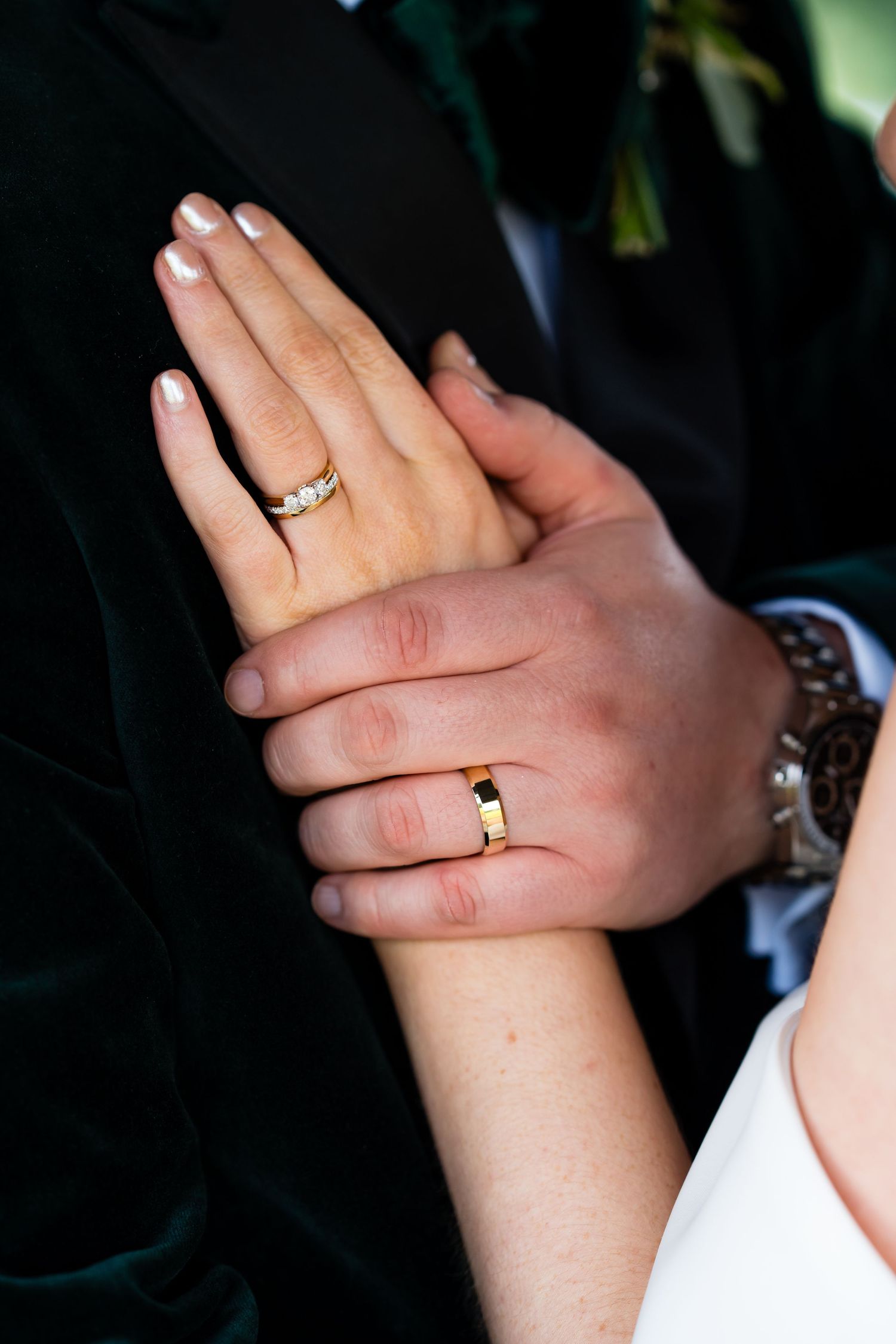 Newlywed couple displaying matching gold wedding rings on their hands, bride in white, groom in dark suit.